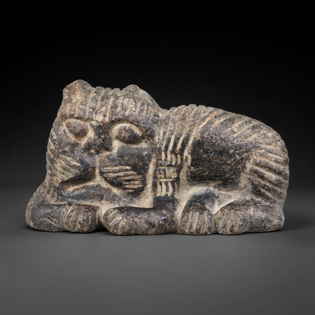 Ancient Babylonian Civilization Recumbent Lion Stone Talisman (1900-600 BCE), 13AK: This carved dark stone recumbent lion talisman originates from Babylonian Civilization of Mesopotamia, representing the revered feline iconography linked to royal power and divine protection within an