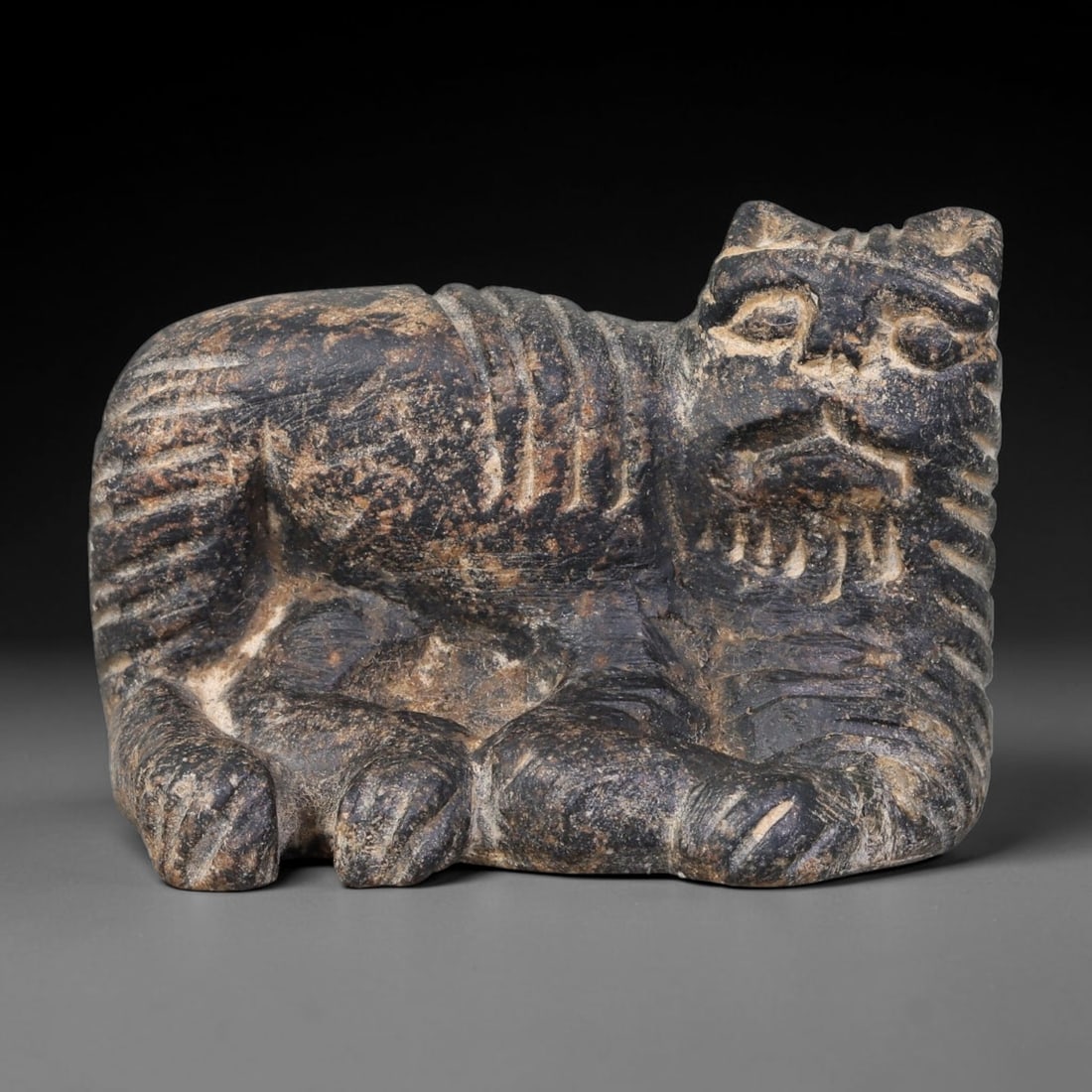 Ancient Babylonian Civilization Recumbent Feline Stone Amulet (1900-600 BCE), 29AK: This carved dark stone recumbent feline amulet originates from Babylonian Civilization of Mesopotamia, serving as a protective talisman invoking feline symbolism associated with guardianship in ancien
