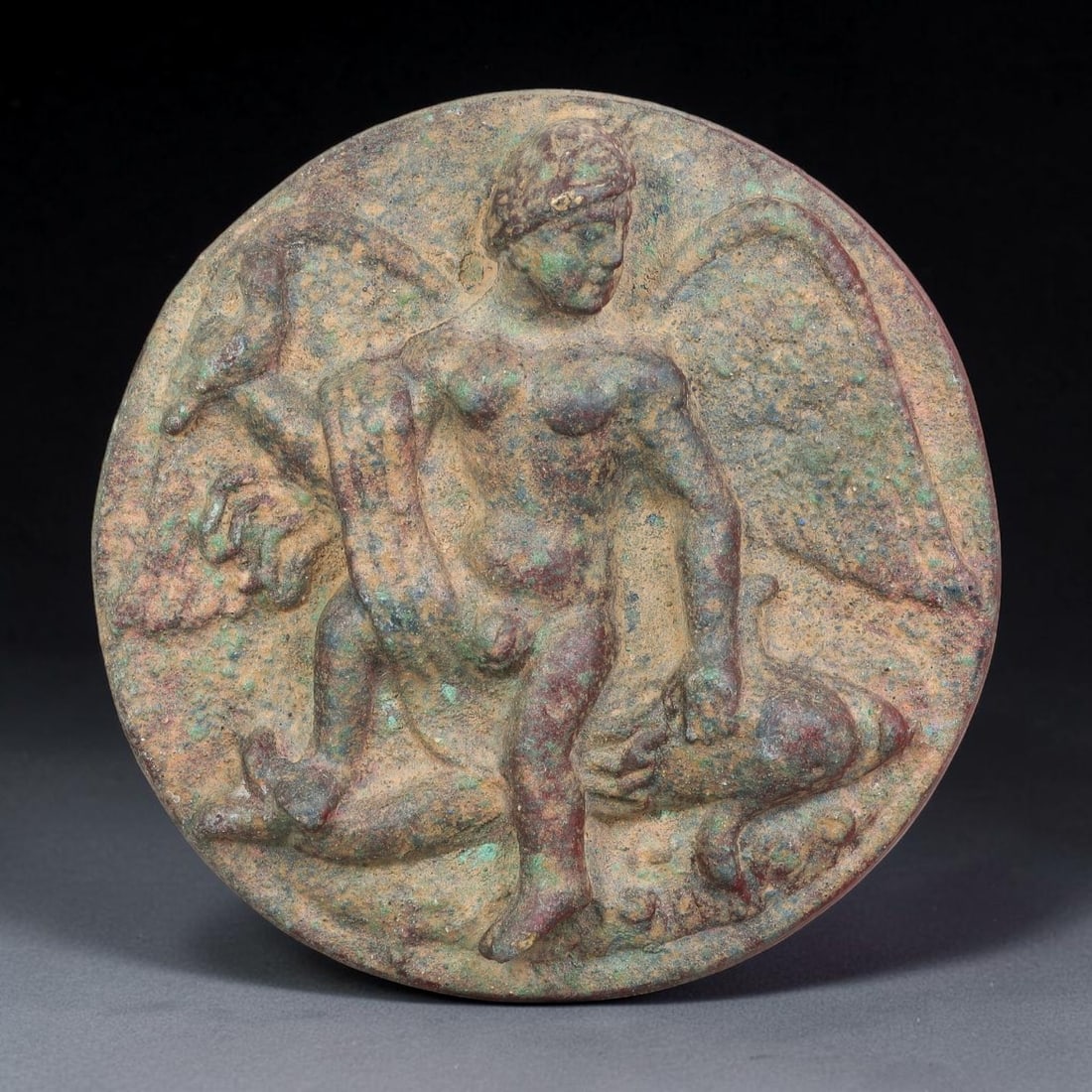 Ancient Greco-Roman Bronze Plaque with Winged Nude Deity on Dolphin, 49AL: Cast bronze plaque with weathered patina of deep brown and pale green mineral deposits. The relief motif depicts a winged nude deity seated atop a dolphin, rendered in classical Greco-Roman iconograph
