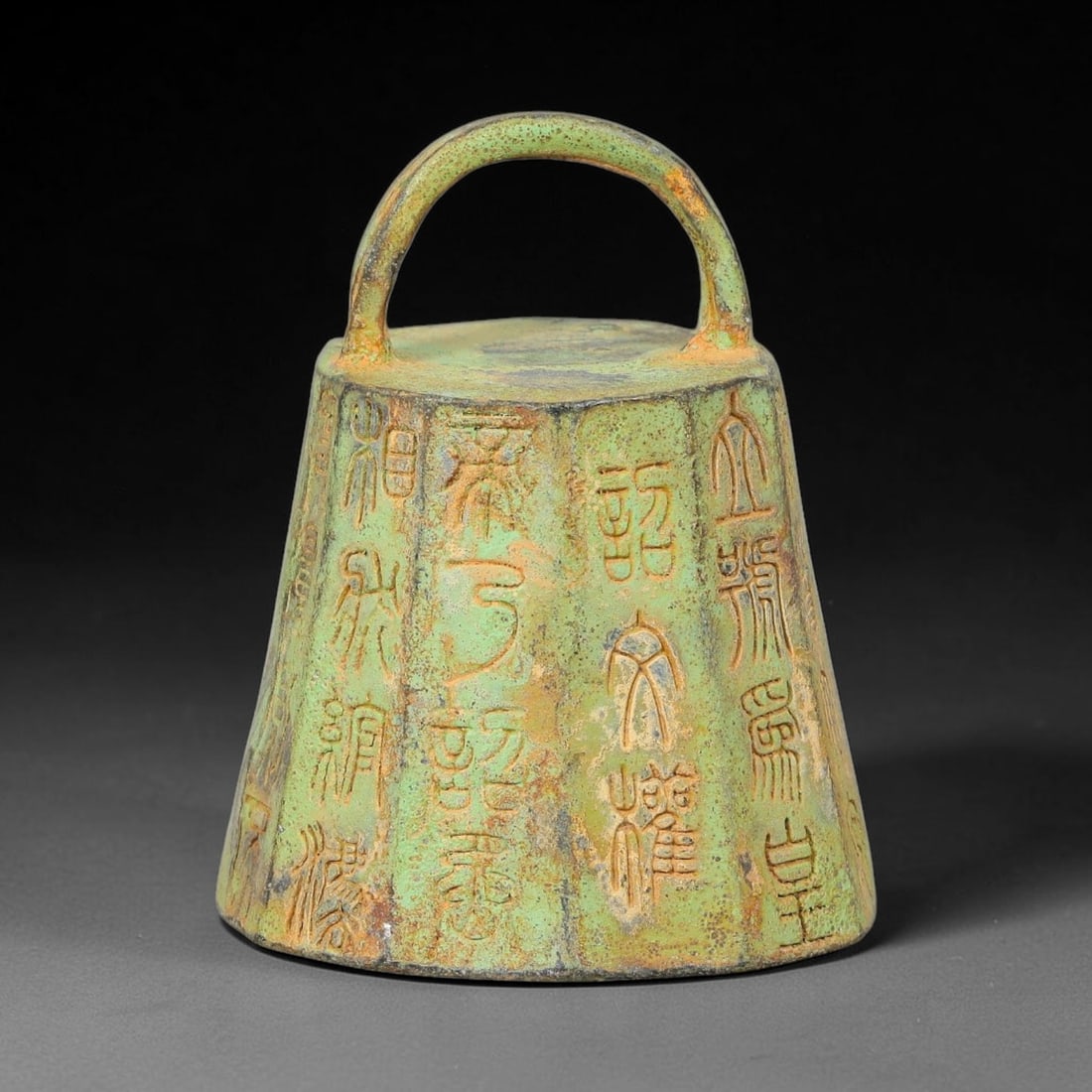 A Chinese Archaic-Style Inscribed Bronze Weight with Loop Handle, 52AD: Cast bronze weight of faceted tapering form, topped by a sturdy integral arched suspension loop. Each vertical facet is deeply incised with archaic seal-script inscriptions covering the outer surface.