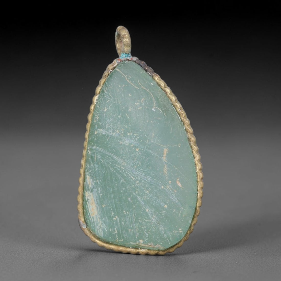 Ancient Roman Glass Slag in Modern Gilt-Edge Pendant, 76AK: This contemporary pendant is crafted from ancient Roman glass slag, featuring a fragmented, iridescent glass surface with weathered patina. The irregular form is bordered by a subtle gilt frame, added