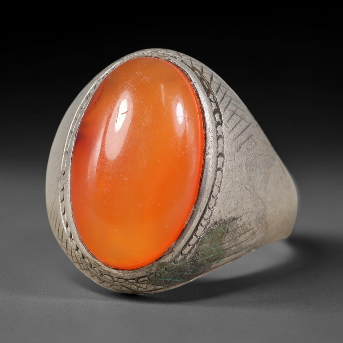 Antique Ottoman Carnelian Dual Border Engraved Silver Ring, 11AL: Silver ring of the Ottoman period set with an oval cabochon carnelian secured within a dual decorative engraved border. The ring shoulders feature fine crisscross geometric engraving. No hallmarks pre