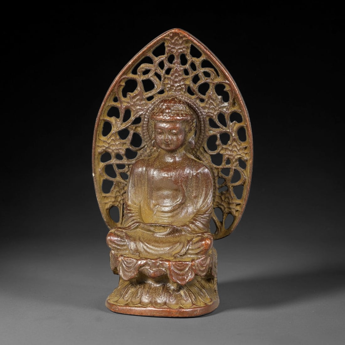 A Chinese Bronze Seated Buddha Figurine with Open-Work Mandorla, 86AD: Cast bronze buddha figure seated in full lotus posture upon layered lotus pedestal. Behind the figure rises a large pointed mandorla backplate with elaborate open-work floral and scrolling foliage pie