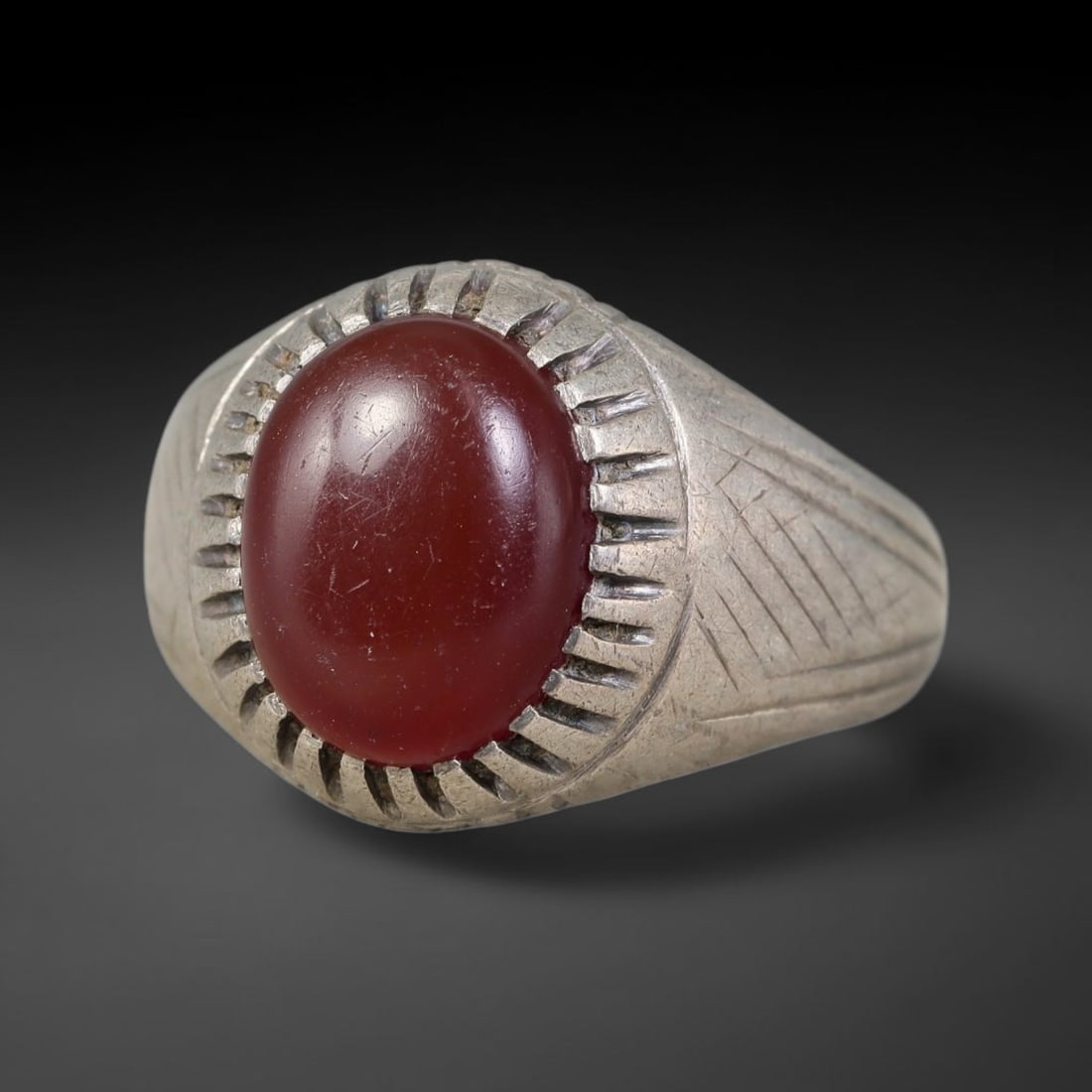 Antique Ottoman Carnelian Radiating Incised Bezel Silver Ring, 14AL: Silver ring of the Ottoman period set with an oval cabochon carnelian secured within a radiating incised bezel. The ring shank bears linear engraved geometric decoration on both shoulders. No hallmark