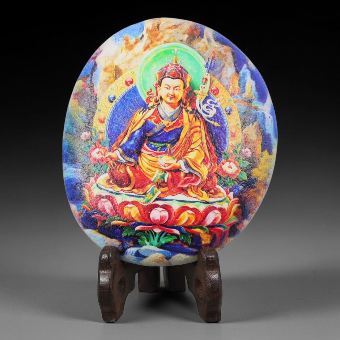 A Tibetan Thangka Style Painted River Stone with a Guru Figure, 71BC: Painted on a naturally rounded, circular river stone, the work depicts a figure of Guru Padmasambhava in a thangka-style composition. The figure is shown seated in a meditative posture upon a lotus th