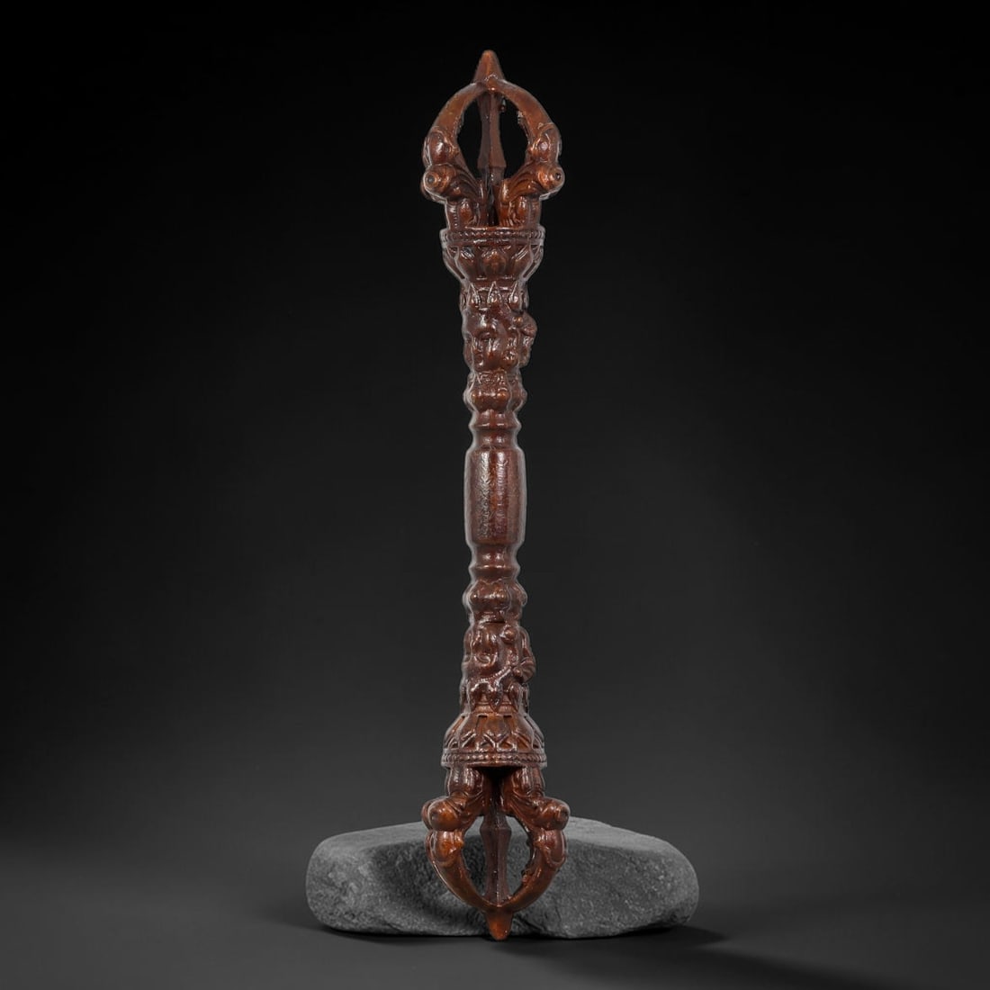 A Chinese Tibetan Bronze Double-Ended Vajra Ritual Implement, 12AJ: Cast in bronze, this elongated double-ended vajra displays multi-pronged open-work vajra terminals at both extremities. The central shaft is densely decorated with deeply-carved lotus foliate and figu