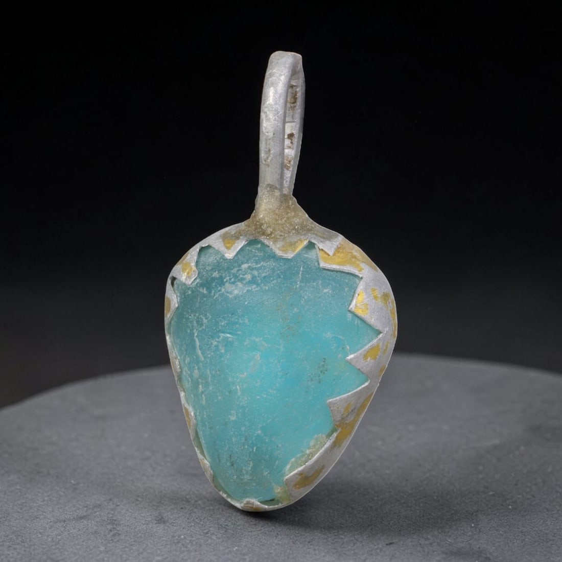 Ancient Roman Glass Slag in Modern Gilt-Edge Pendant, 74AK: This contemporary pendant is crafted from ancient Roman glass slag, featuring a fragmented, iridescent glass surface with weathered patina. The irregular form is bordered by a subtle gilt frame, added
