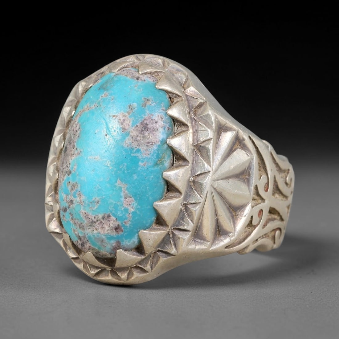 Antique Ottoman Turquoise Starburst Engraved Serrated Bezel Silver Ring, 16AL: Silver ring of the Ottoman period set with an oval cabochon turquoise secured within a serrated bezel. The shoulder is decorated with carved starburst motif and scroll openwork detailing. Marked with 
