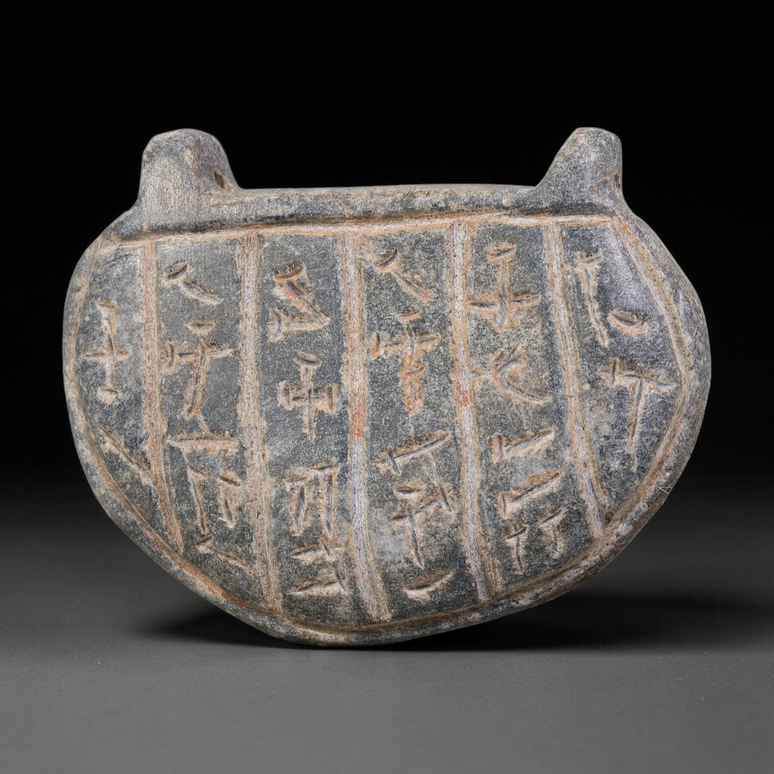 Ancient Uruk Period Oval Inscribed Apotropaic Amulet (c.3500-3100 BCE), 99AJ: Oval-shaped apotropaic amulet from the Uruk cultural sphere, with two integrated suspension lugs positioned at the upper edge to allow personal suspension. The front face is divided into vertical comp