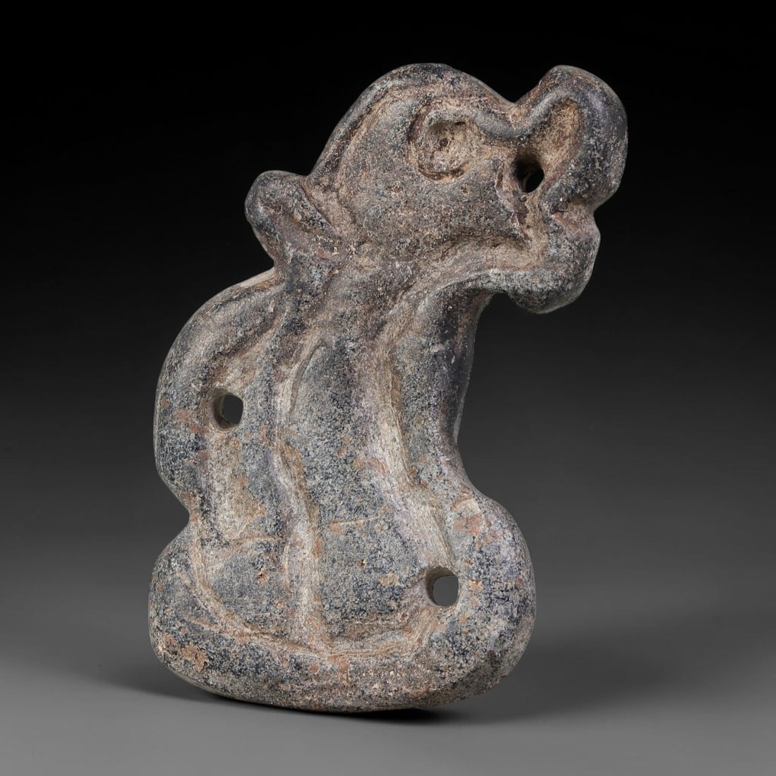 Ancient Elamite Civilization Serpent-Form Multi-Perforated Stone Amulet (3200-539 BCE), 97AJ: This carved dark mottled stone amulet originates from Elamite Civilization, shaped as a stylized serpent figure with multiple drilled perforations for suspension and attachment. Soft relief carving de