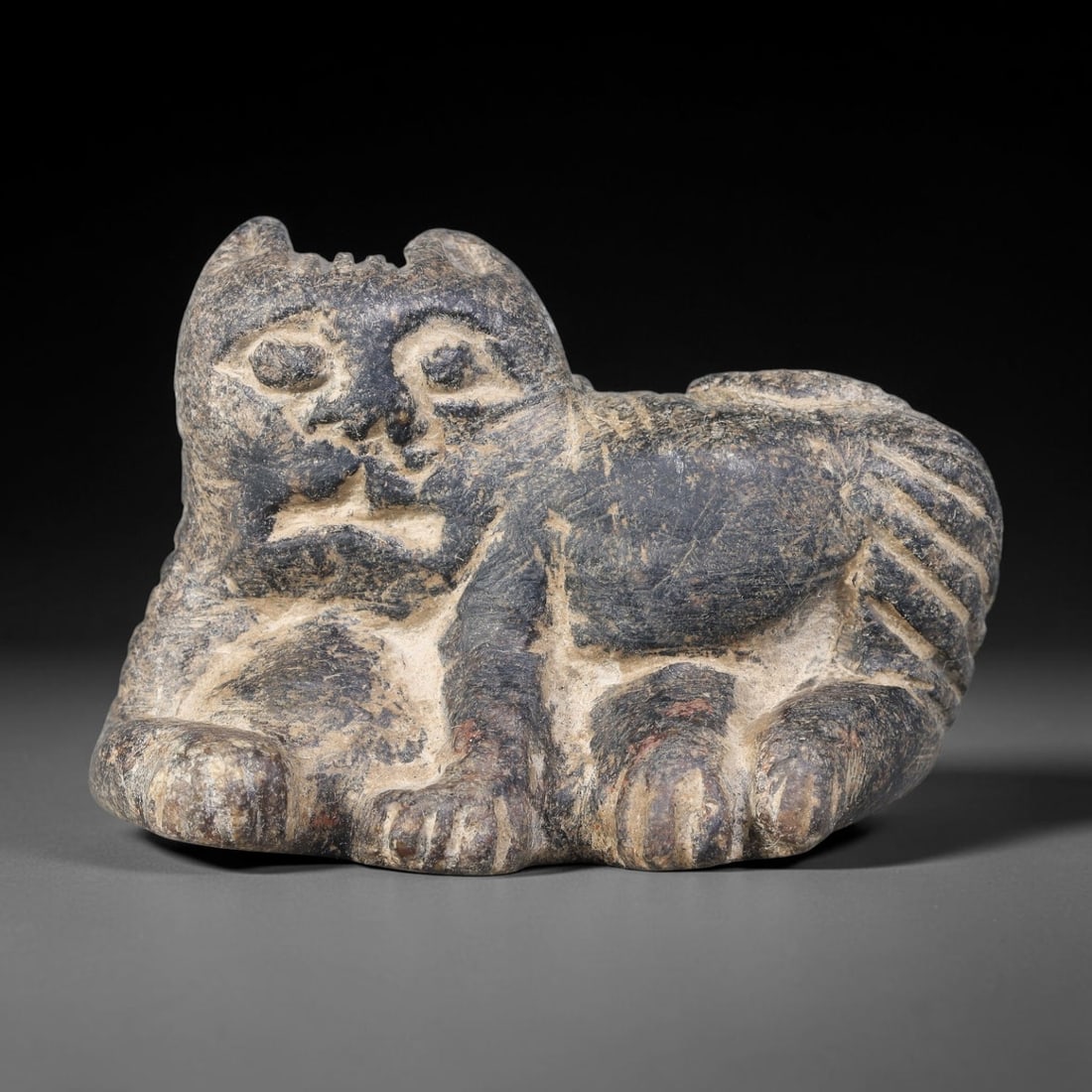 Ancient Sasanian Persian Schist Recumbent Feline Amulet (224-651 CE), 57AJ: Talismanic schist stone carving representing a recumbent feline creature, executed in Sasanian Persian sculptural idiom. Bold deep incised lines render facial features, paws and striped tail, embodyin