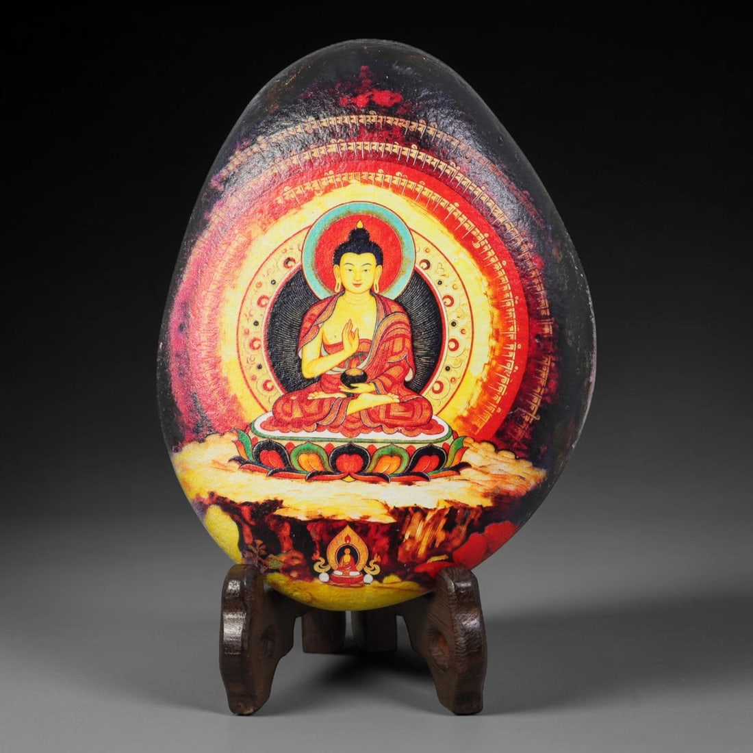 A Tibetan Thangka Style Painted River Stone with a Buddhist Figure, 58BC: Painted on a naturally rounded river stone with a smooth, granular surface, the work depicts a seated Buddhist figure in a thangka-style composition. The figure is shown in a meditative posture upon a