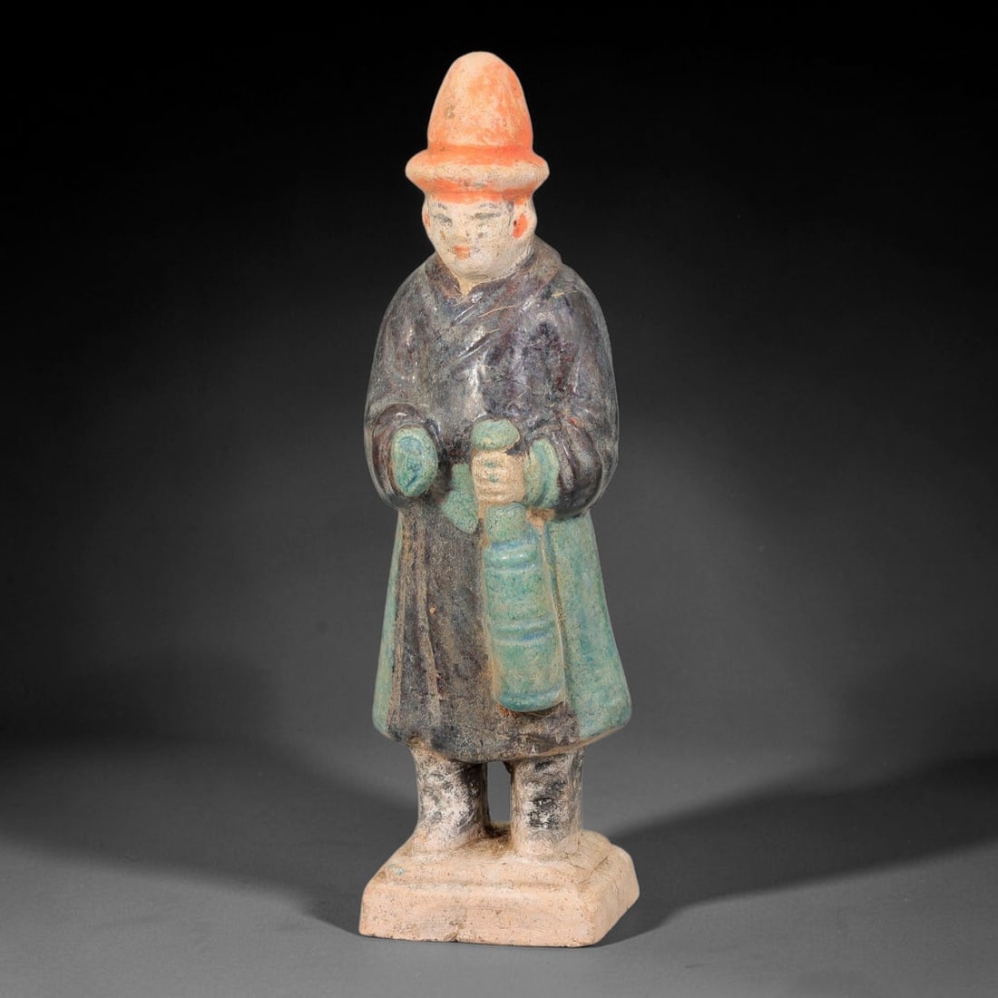 A Chinese Ming Dynasty Glazed Terracotta Male Attendant Figurine, 82AL: Modelled in hollow terracotta, the standing male attendant retains polychrome glaze and pigment. The figure wears a conical hat with orange-red pigment, and defined facial features with pigmented lips