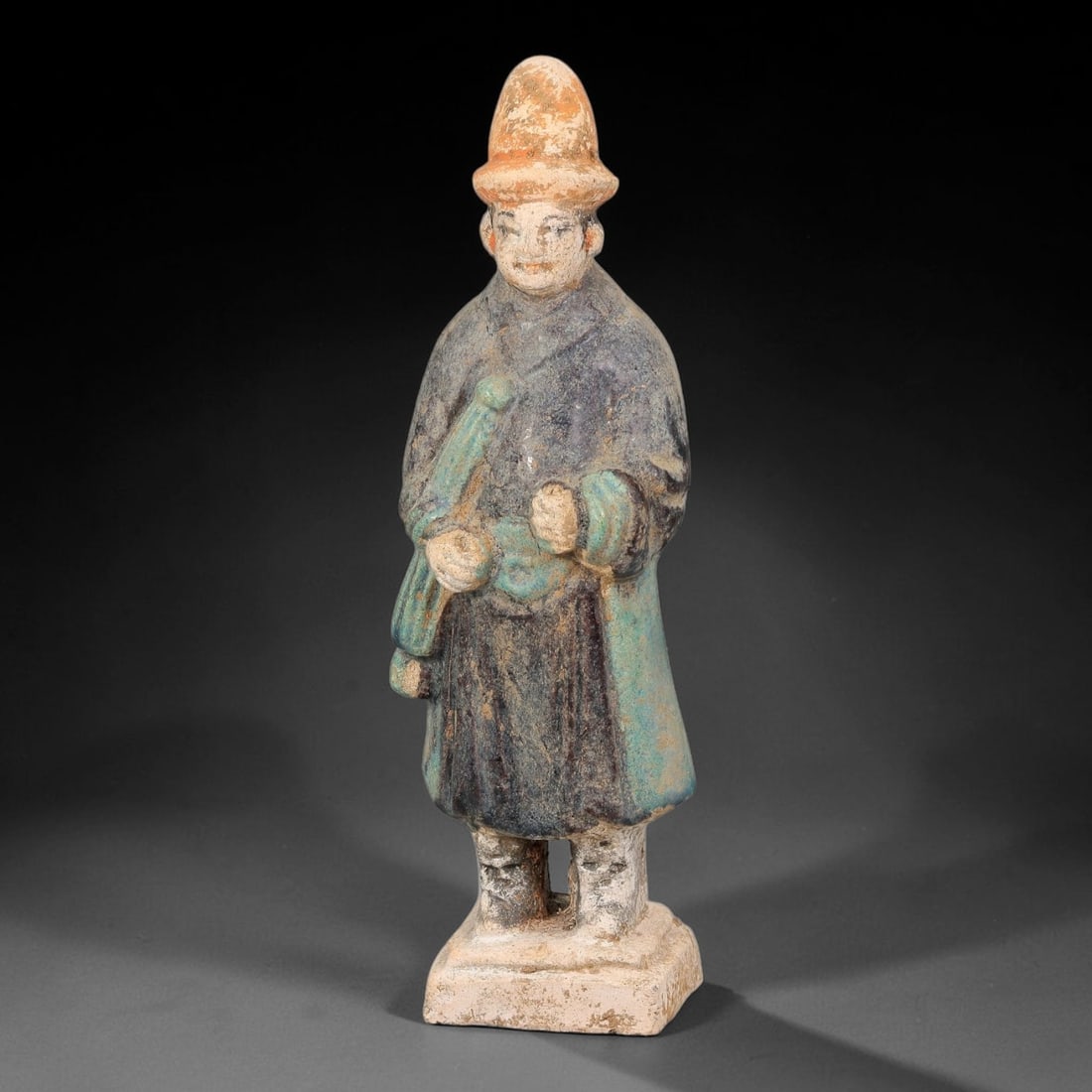 A Chinese Ming Dynasty Glazed Terracotta Male Attendant Figurine, 84AL: Modelled in hollow terracotta, the standing male attendant retains polychrome glaze and pigment. The figure wears a conical hat with orange-red pigment at the brim, and defined facial features with pi