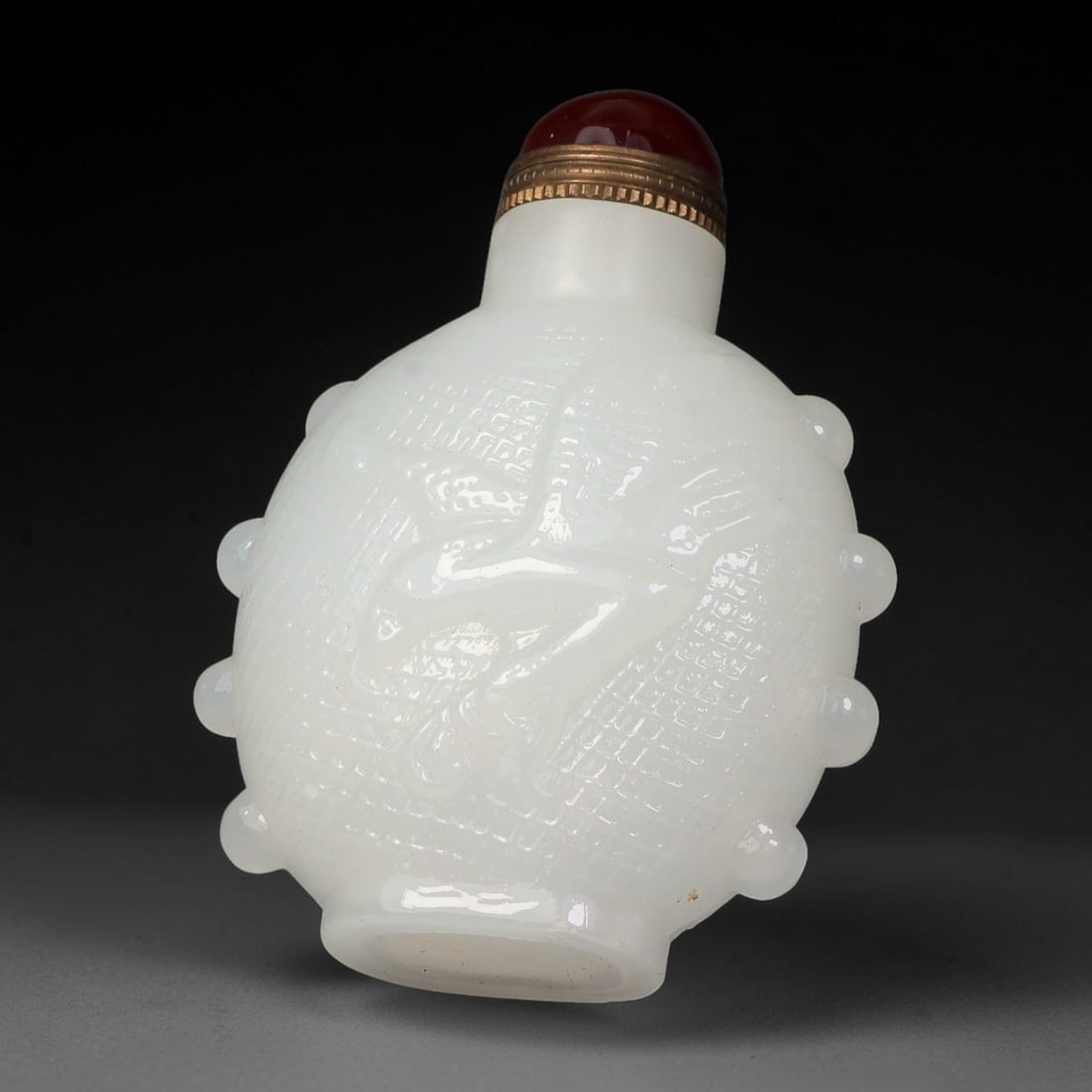 A Chinese White Peking Glass Relief Carved Snuff Bottle, 59AV: Ovoid snuff bottle crafted from smooth white Peking glass, featuring central raised relief carving upon a woven textured ground, surrounded by evenly spaced rounded bosses around the perimeter. It is 