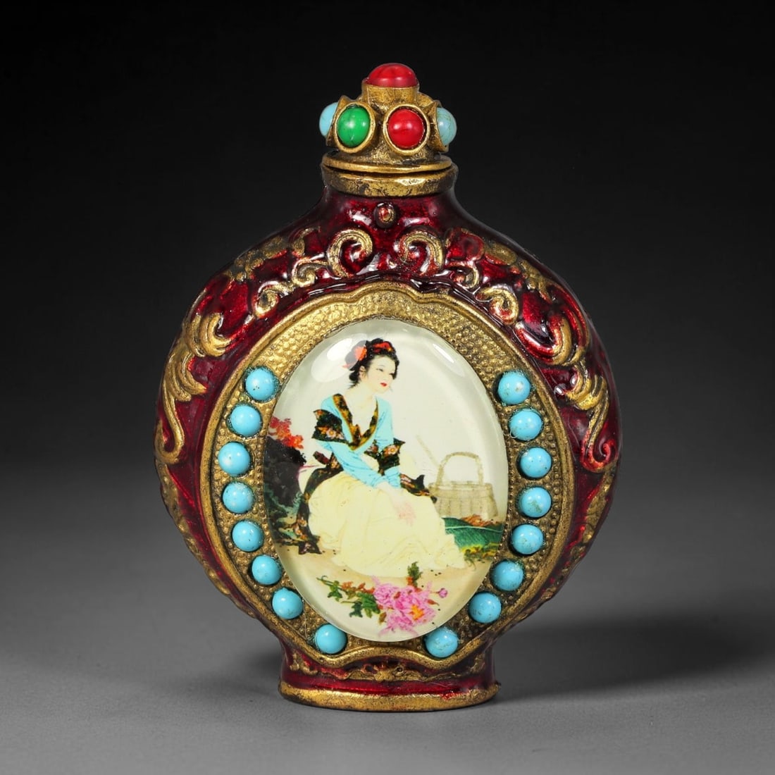 A Chinese Gilt Copper Alloy Inset Painted Panel Snuff Bottle, 29AV: Modelled in gilt copper alloy with deep red enamel and raised gilt scroll relief decoration, the snuff bottle has a flattened ovoid form fitted with a stopper set with simulated coral, green and turqu