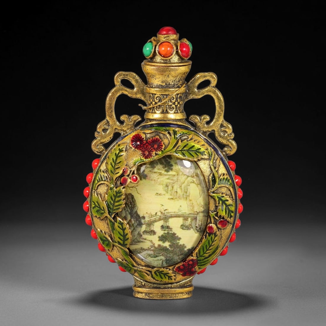 A Chinese Gilt Copper Alloy Two-Handled Inset Painted Panel Snuff Bottle, 31AV: Modelled in gilt copper alloy, the snuff bottle features a flattened ovoid body fitted with a pair of elaborate scrolling handles and a stopper set with simulated coral, orange and green cabochons. Th