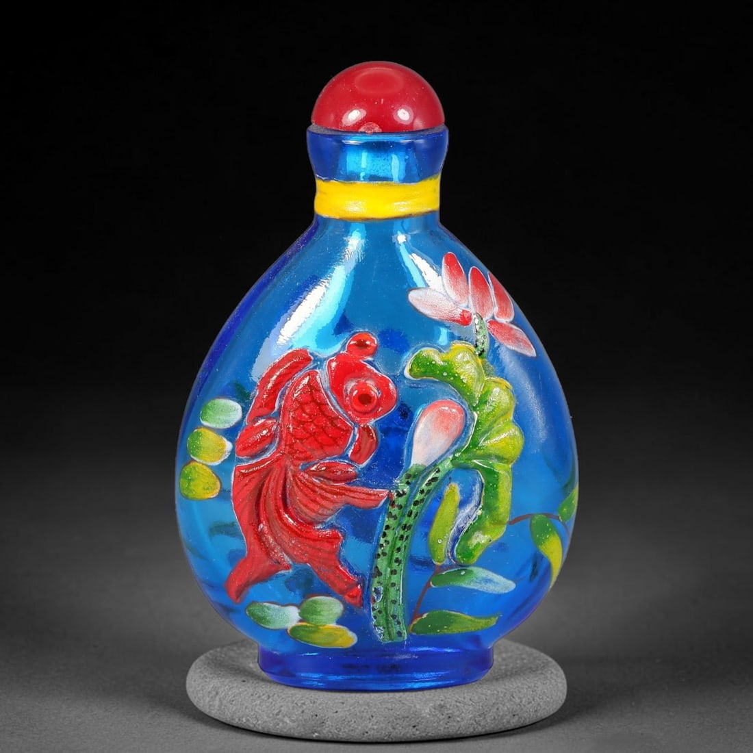 A Chinese Blue Glass Overlay Enamel Fish and Lotus Snuff Bottle, 7AV: Pear-shaped translucent blue glass snuff bottle decorated in raised overlay enamel style with opposing fish and lotus motifs. One side shows a bright red carp amid green water weeds, lily pads and pin