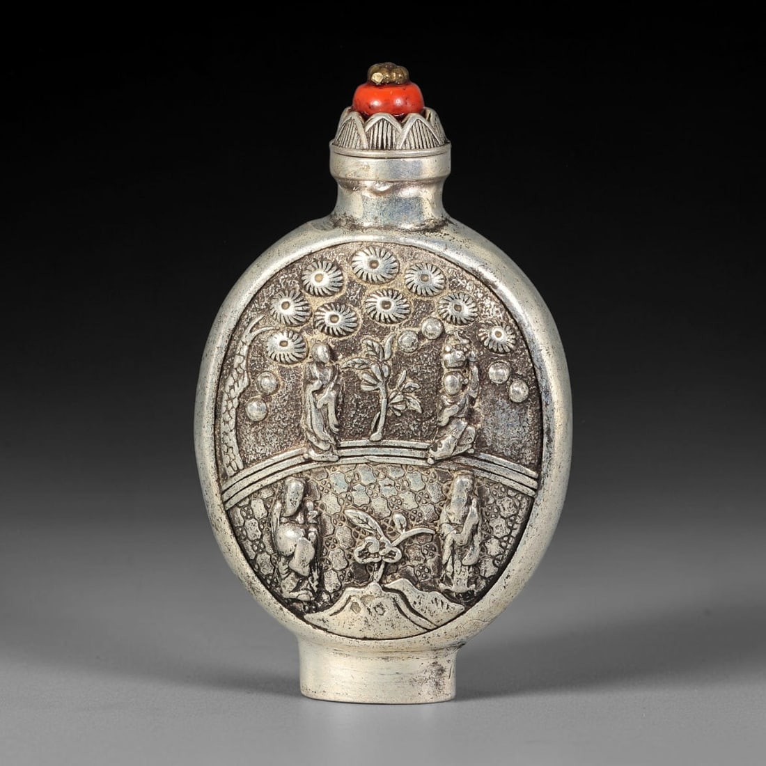 A Chinese Repousse Metal Figural Snuff Bottle, 61AV: Moon flask shaped snuff bottle with raised repousse figural landscape decoration, depicting robed scholars beneath flowering trees on both sides, set against a textured stippled background. The bottle