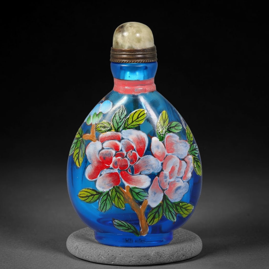 A Chinese Sky Blue Glass Enamel Peony Snuff Bottle, 48AV: Pear-shaped translucent sky blue glass snuff bottle decorated with hand-painted polychrome enamel peony blooms and lush foliage. A narrow red band encircles the neck, fitted with brass mounting and a 