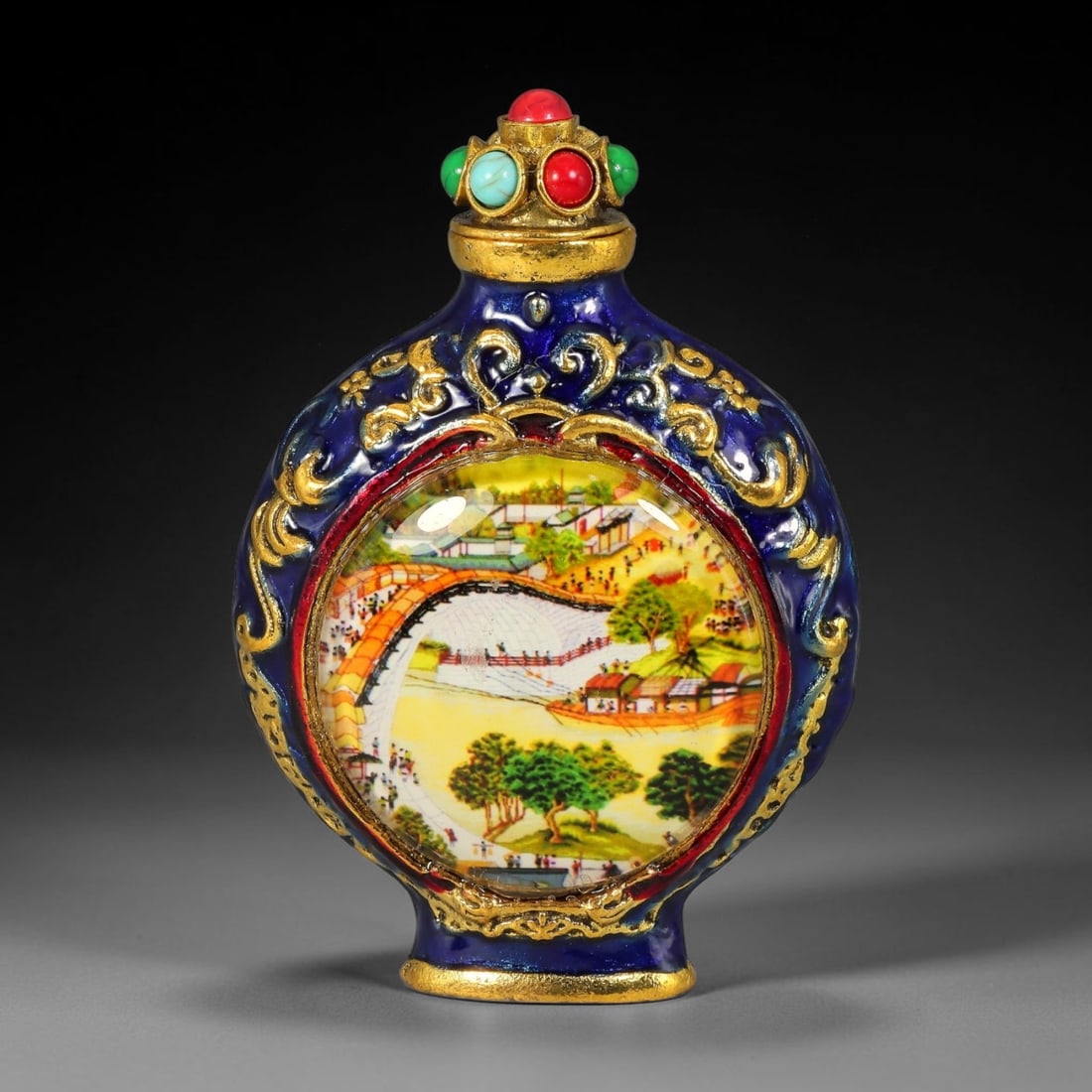 A Chinese Gilt Metal Blue Enamel Snuff Bottle Riverside Scene at Qingming Festival Panels, 40AV: Flattened circular snuff bottle crafted in gilt metal with deep cobalt blue enamel and raised gilt scrolling foliate ornamentation surrounding each circular domed inset panel. The stopper is set with 