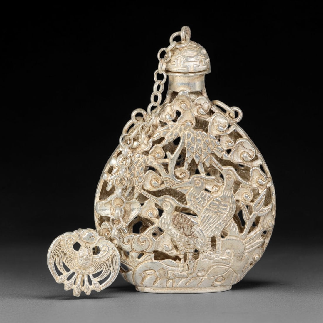A Chinese German Silver Double-Sided Openwork Snuff Bottle, 65AV: Pear-shaped German silver snuff bottle with elaborate double-sided openwork carving. One face features cranes amid pine and cloud scrolls; the reverse depicts a bird among lotus blossoms and flowering
