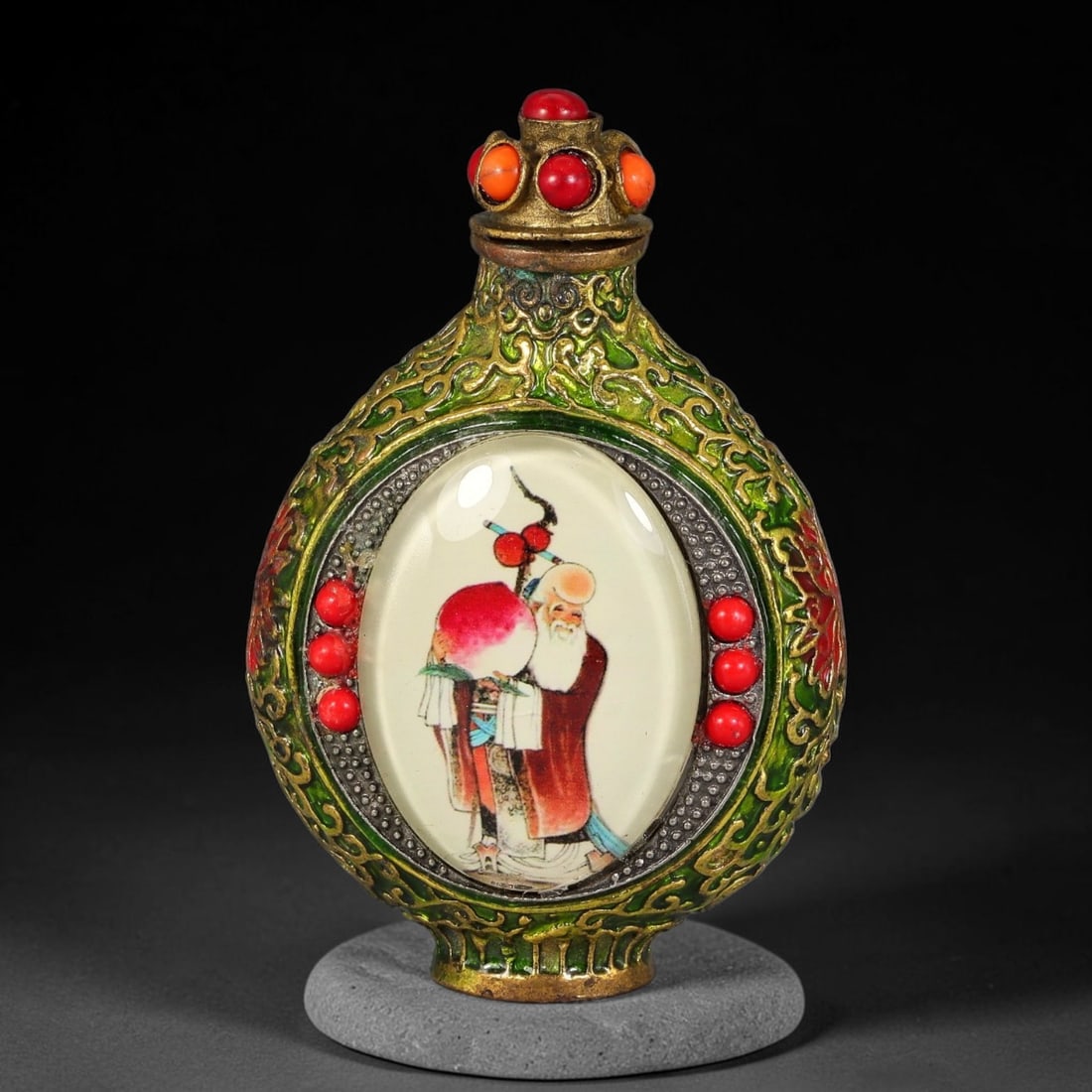 A Chinese Gilt Copper Alloy Inset Painted Panel Snuff Bottle, 32AV: Modelled in gilt copper alloy with green enamel and raised gilt scroll ornamentation, the snuff bottle has a flattened ovoid form with a fitted stopper set with simulated coral and orange cabochons. E