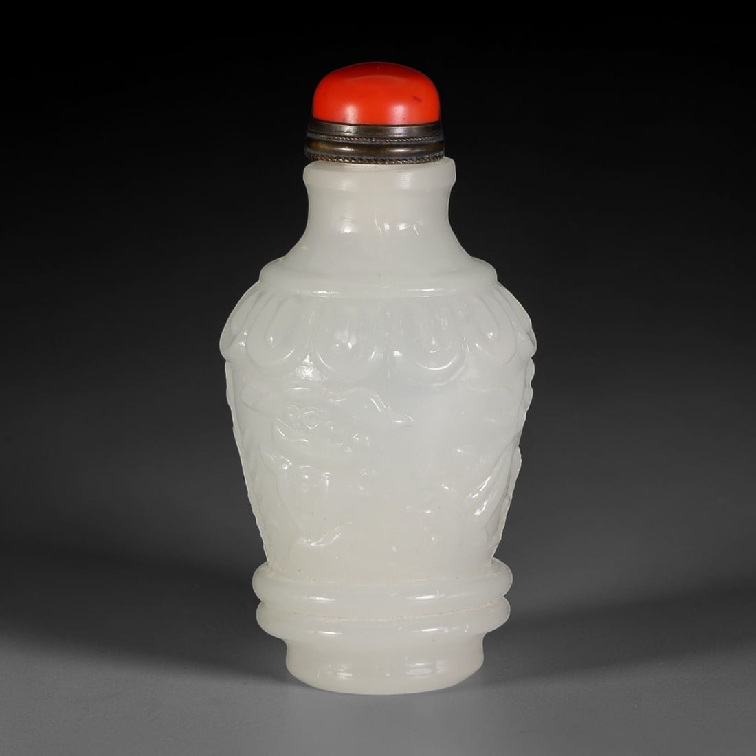 A Chinese White Peking Glass Carved Snuff Bottle, 58AV: Baluster-form snuff bottle crafted from smooth white Peking glass, decorated with raised relief carving of stylized motifs beneath a band of petal detailing around the shoulder. The bottle is fitted w