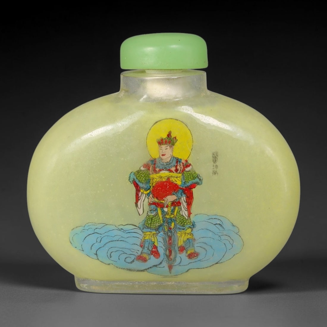 A Chinese Inside Painted Glass Snuff Bottle with Heavenly Guardian Motif, 80AV: Flattened globular glass snuff bottle with pale translucent yellow ground, finely decorated with interior painting depicting a heavenly guardian deity standing atop billowing blue clouds, crowned with