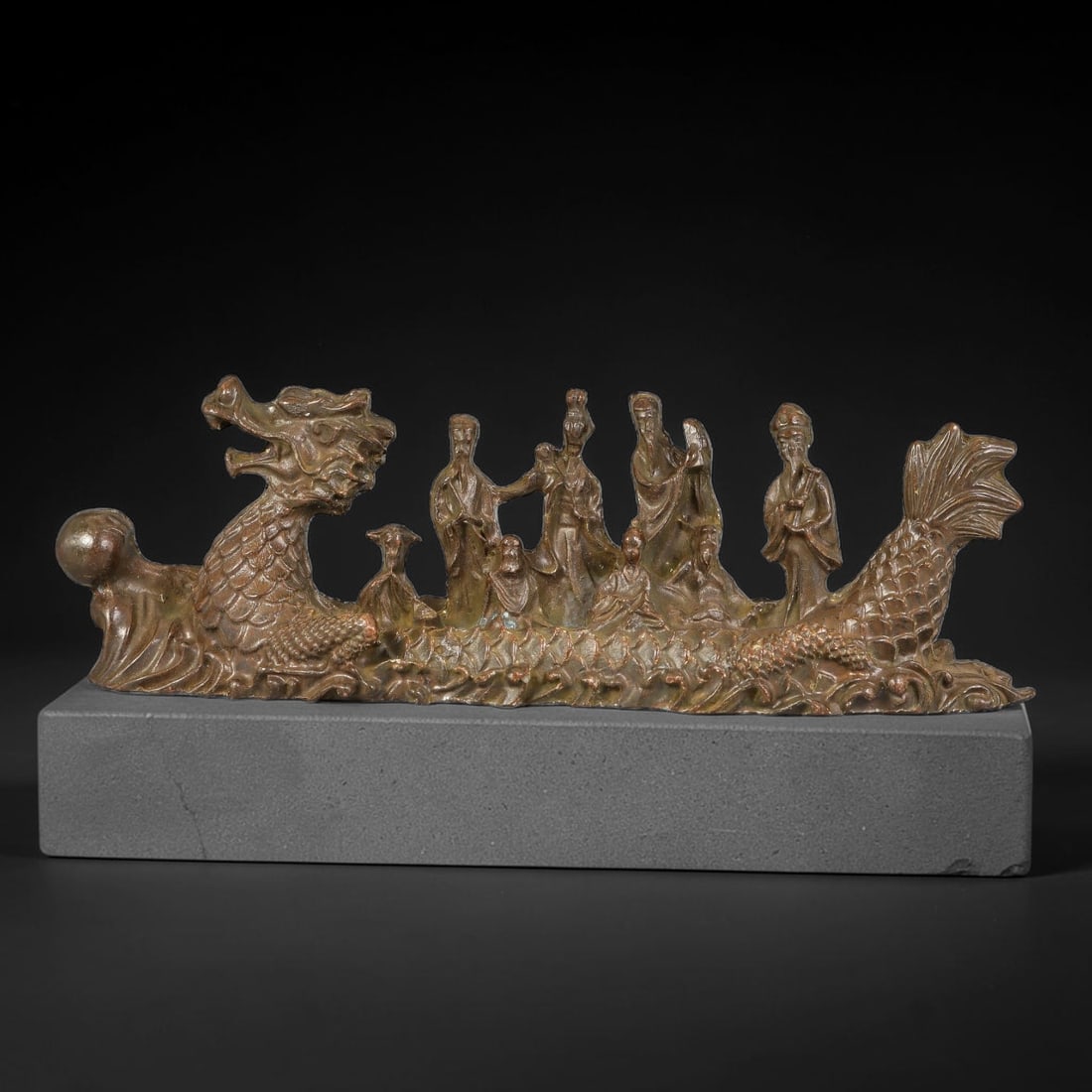 A Chinese Bronze Group of Eight Immortals on Dragon Boat, 9AX: Cast bronze sculpture depicting the Eight Immortals aboard a detailed dragon boat, with scaled dragon head at the bow and finned tail at the stern, all figures finely modelled in traditional robes. He