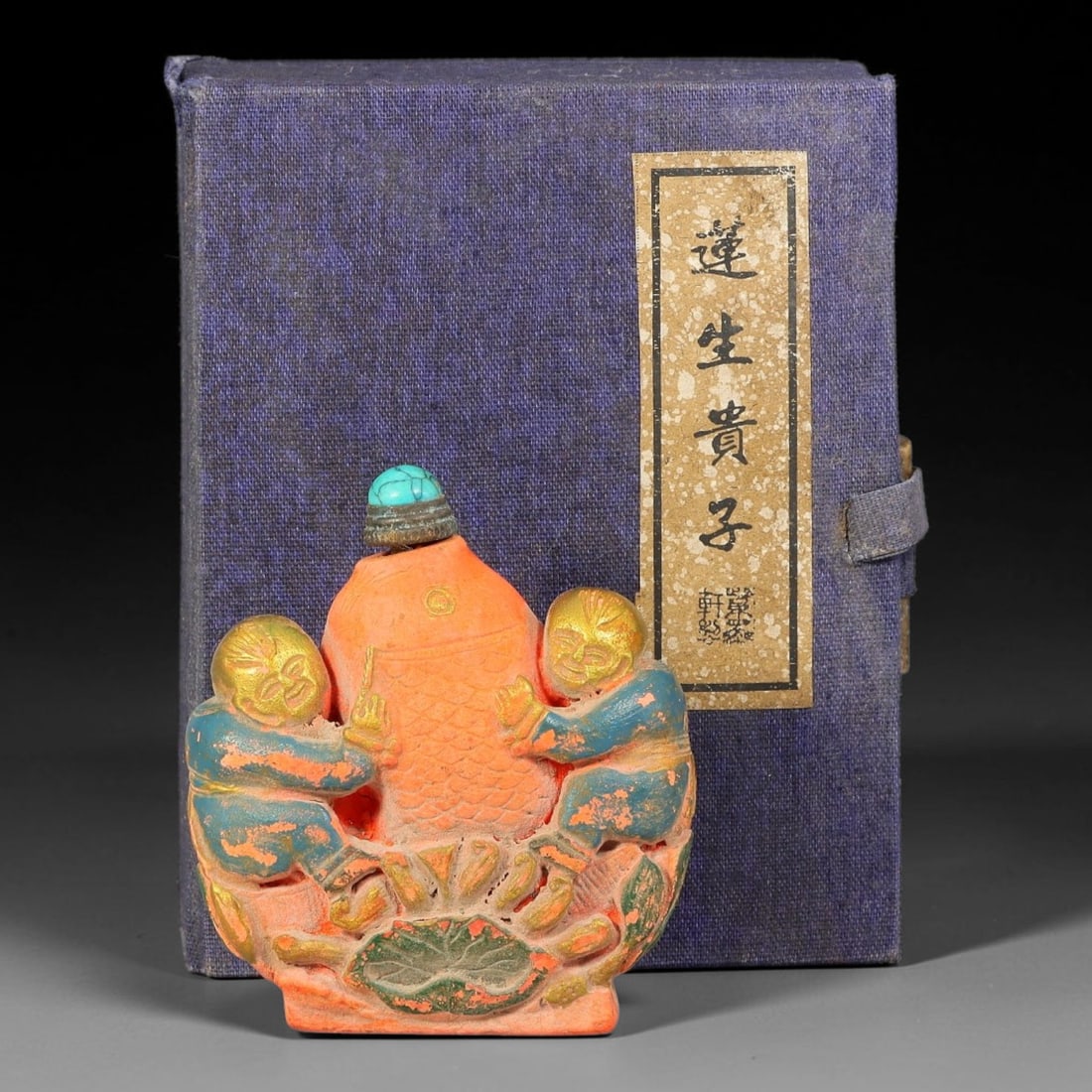 A Chinese Painted Relief Carved Boys and Carp Snuff Bottle with Original Box, 2AX: Figural form snuff bottle, modelled as two boys embracing a large carp rising from lotus foliage, decorated with polychrome pigment and gilded highlights. The vessel is fitted with a turquoise cabocho