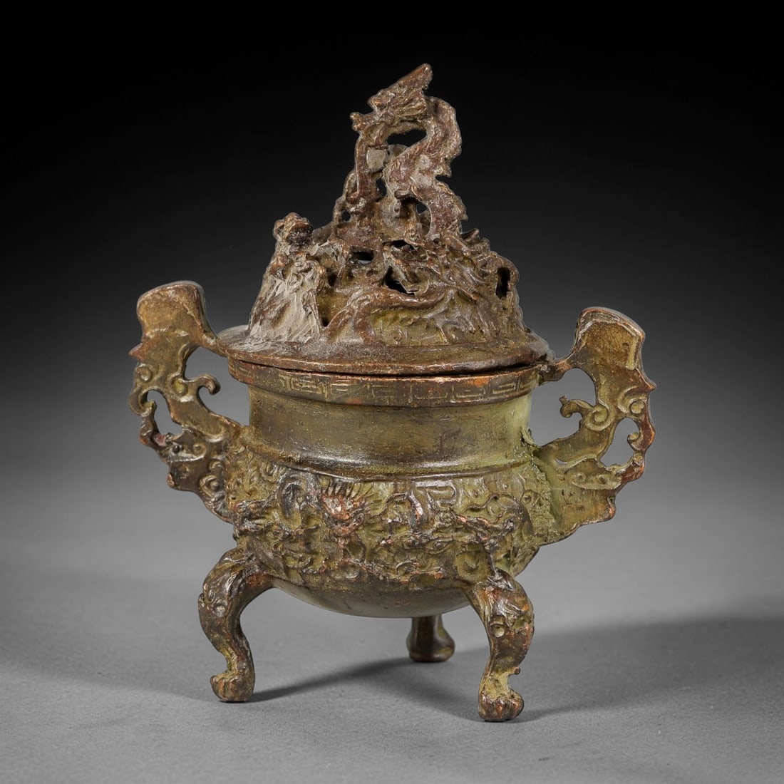 A Chinese Bronze Tripod Censer with Openwork Dragon Mountain Lid, 12AX: Cast bronze tripod censer with rich relief dragon ornamentation. The elaborate openwork lid is modelled as a rocky mountain scene intertwined with coiled dragons for smoke dispersion. The rounded body