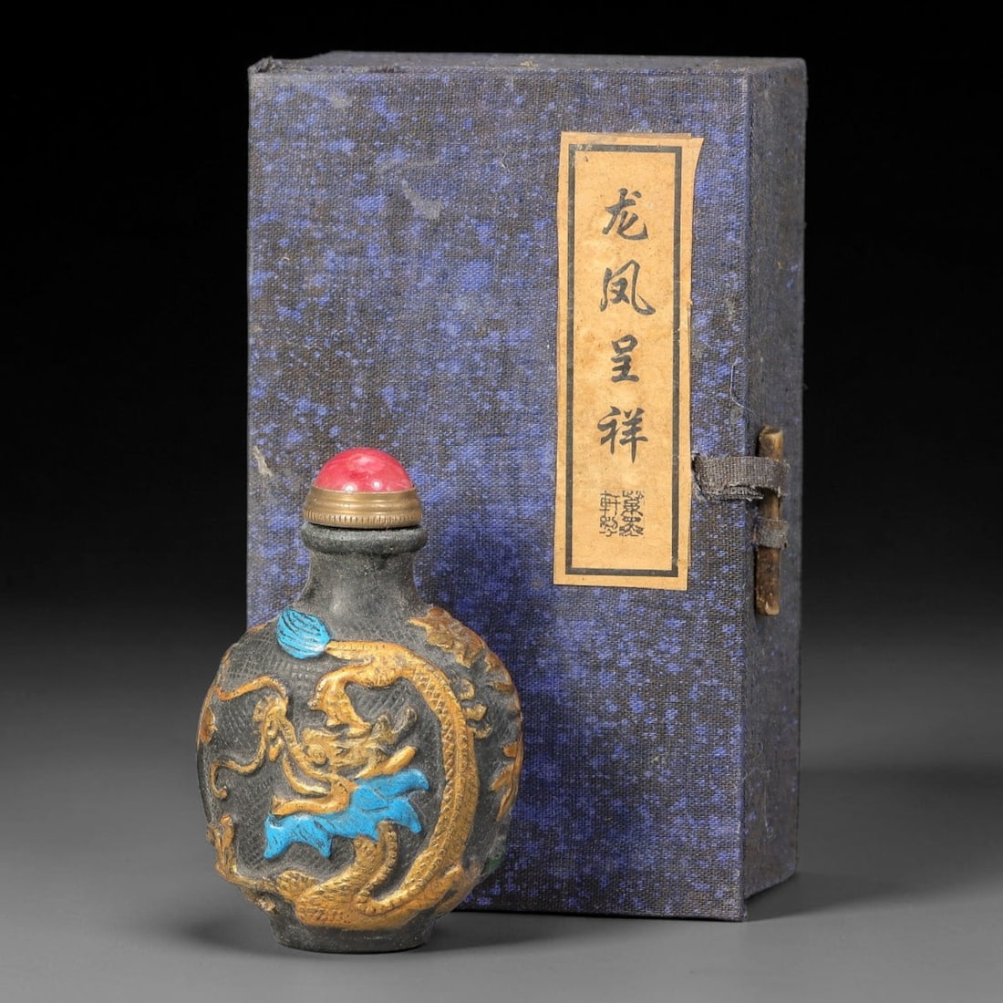 A Chinese Painted Relief Carved Dragon and Phoenix Snuff Bottle with Original Box, 76AV: Globular snuff bottle of dark toned material, decorated with polychrome raised relief carving, one side depicting a phoenix and peony, the reverse showing a dragon amid cloud and scroll motifs, the ba
