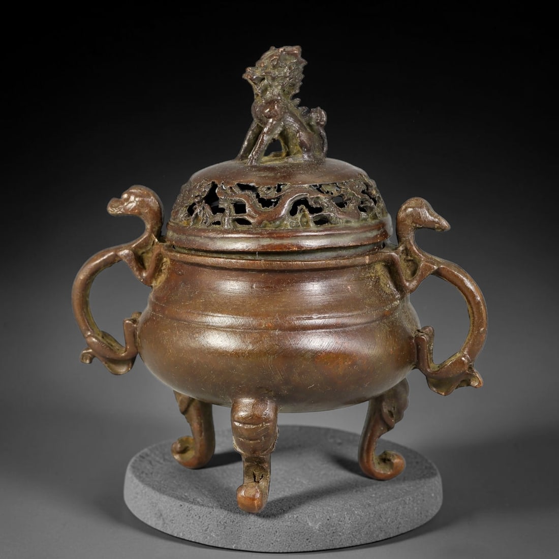A Chinese Bronze Tripod Censer with Qilin Finial and Openwork Lid, 11AX: Cast bronze tripod censer with a smoothly rounded bulbous body. The domed openwork lid features pierced foliate cutouts and is surmounted by a seated qilin finial. Twin serpentine beast-form handles e