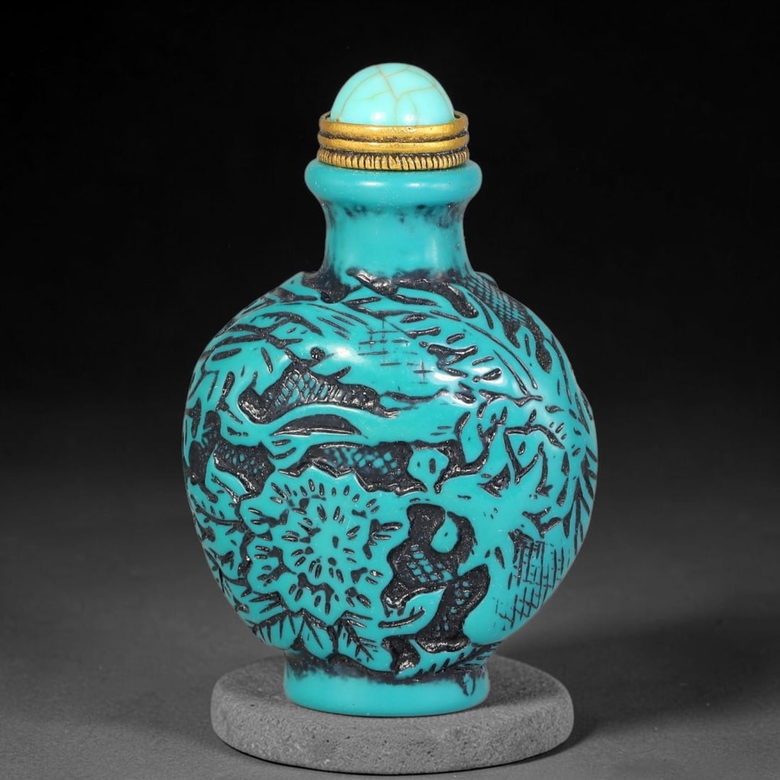 A Chinese Turquoise and Black Relief Carved Floral and Fish Snuff Bottle, 94AV: Globular snuff bottle with turquoise relief carving over dark recessed ground, decorated with swimming fish and large floral blooms interspersed with foliage. The vessel is fitted with a cracked turqu