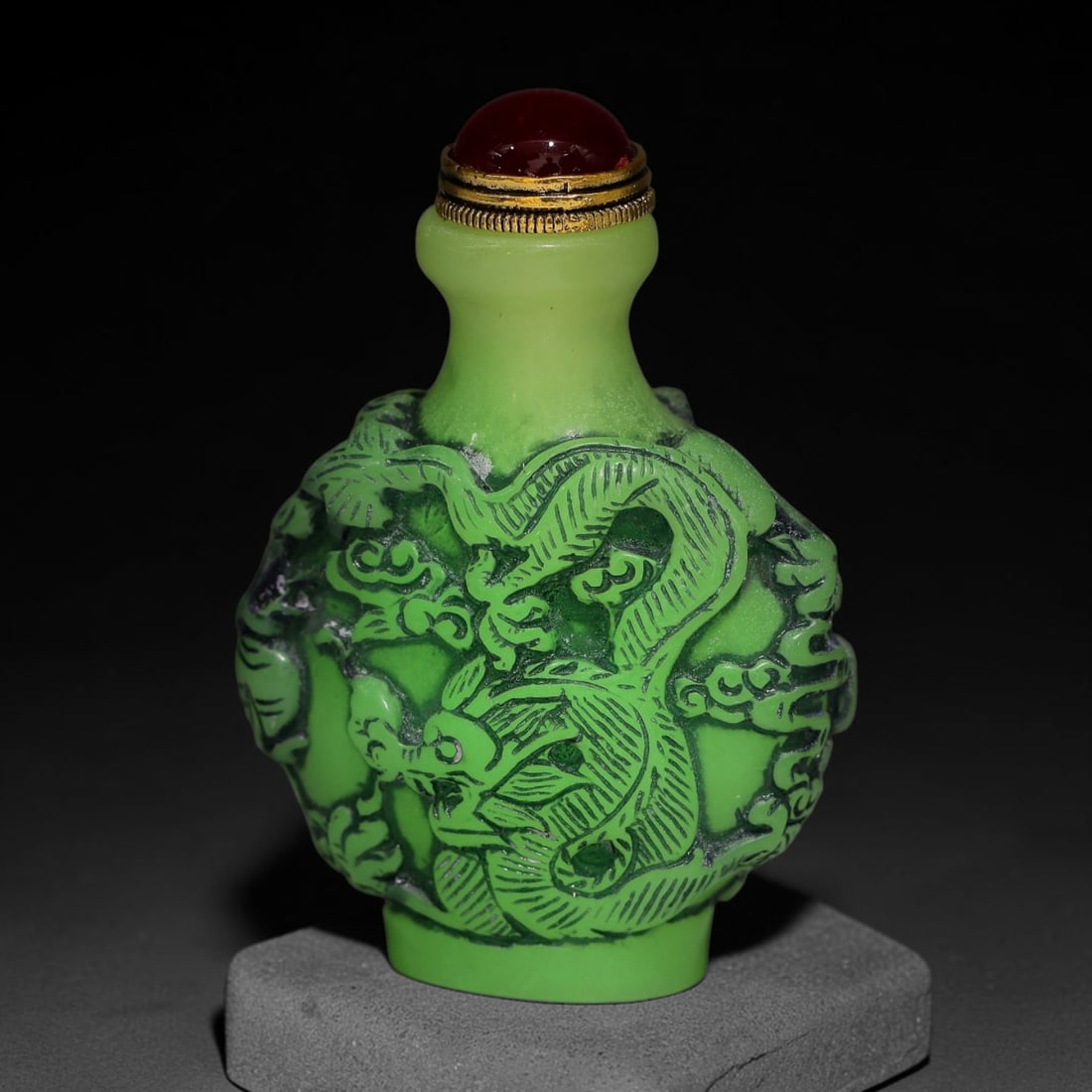 A Chinese Phosphorescent Green Relief Carved Dragon and Phoenix Snuff Bottle, 91AV: Globular phosphorescent green snuff bottle, the material glows neon in the dark when illuminated by torch light, deeply relief-carved with dragon and phoenix winding through cloud scroll ornamentation