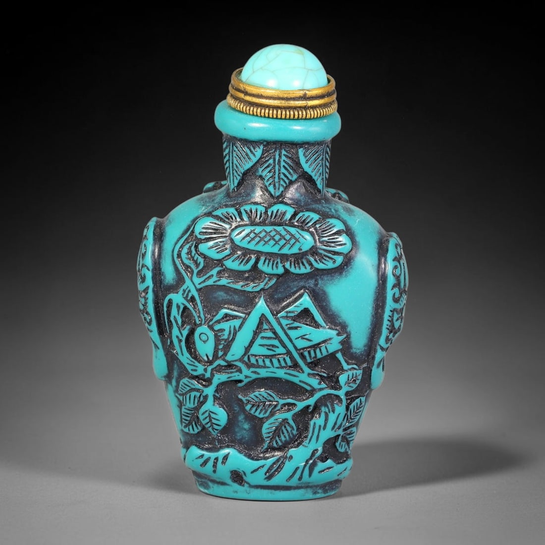 A Chinese Turquoise and Black Relief Carved Landscape Snuff Bottle, 95AV: Baluster-form snuff bottle with turquoise relief carving over dark recessed ground, depicting a landscape scene with pavilion, flowering branches and foliage. Leaf ornamentation decorates the neck, an