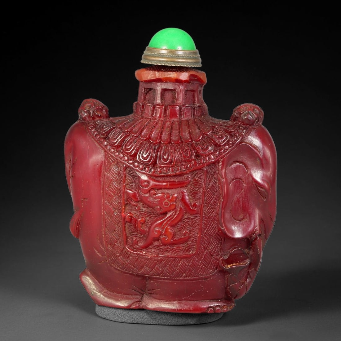 A Chinese Carved Red Snuff Bottle in Elephant Form, 82AV: Elephant-form carved red snuff bottle with relief carved qilin motif set within a textured rectangular panel on the body, flanked by detailed elephant head and trunk elements at the shoulders. The bot