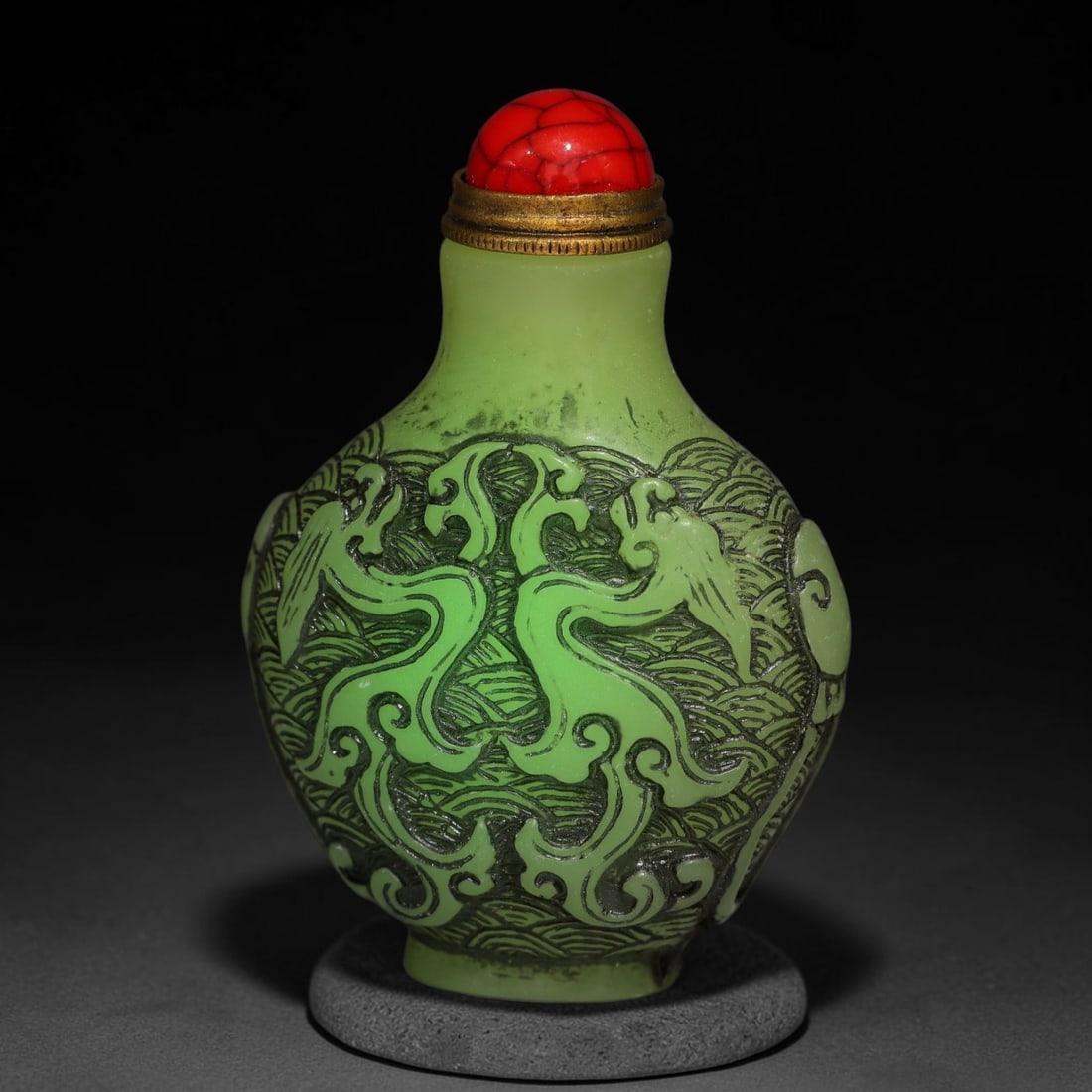 A Chinese Phosphorescent Green Relief Carved Twin Dragon Snuff Bottle, 90AV: Ovoid phosphorescent green snuff bottle, the material glows neon in the dark when illuminated by torch light, deeply relief-carved with twin dragons swirling amid stylized wave patterns across the bod