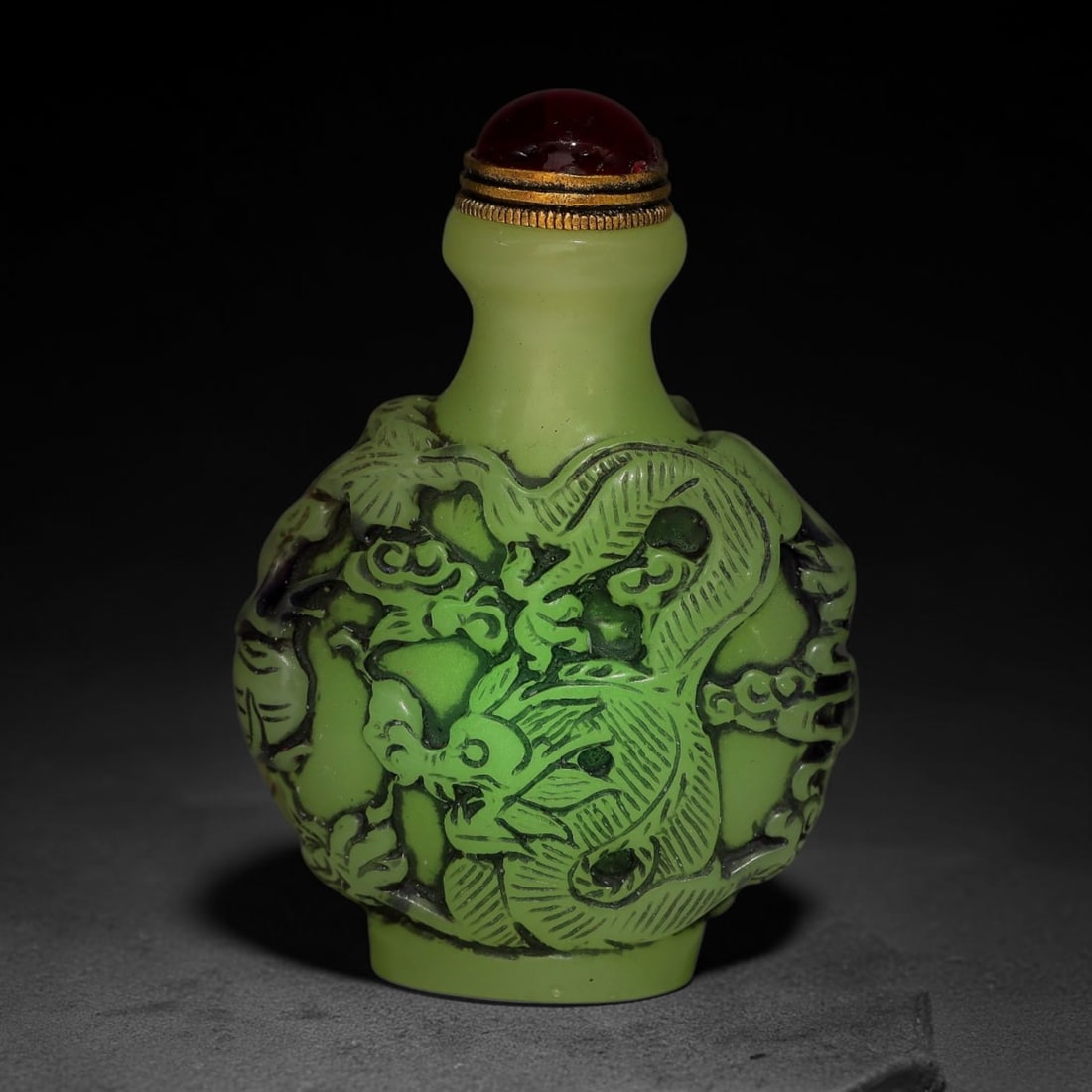A Chinese Phosphorescent Green Relief Carved Dragon Snuff Bottle, 88AV: Globular phosphorescent green snuff bottle, the material glows neon in the dark when illuminated by torch light, deeply relief-carved with a dragon winding through cloud scroll and foliate ornamentati