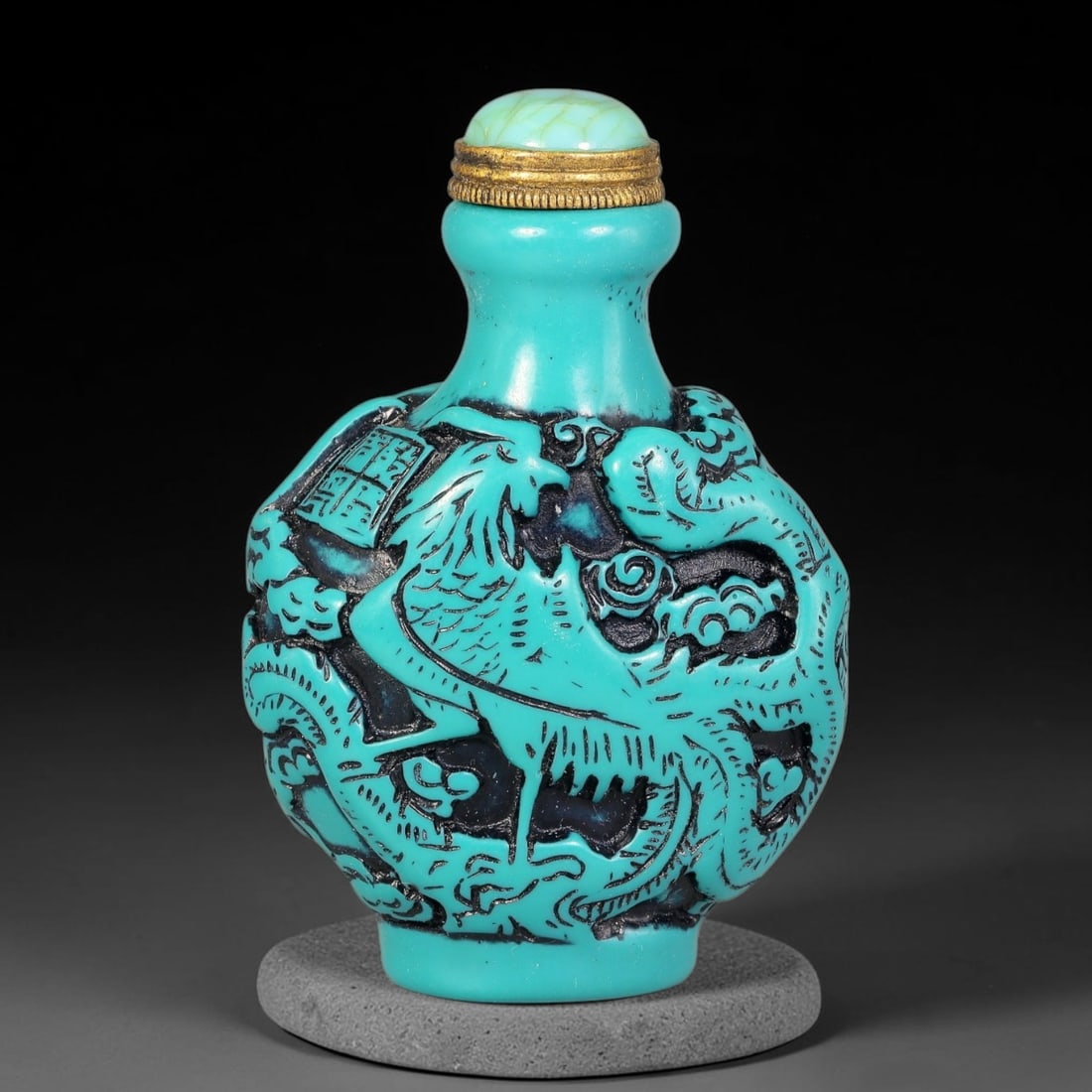 A Chinese Turquoise and Black Relief Carved Dragon and Phoenix Snuff Bottle, 93AV: Globular snuff bottle with turquoise relief carving over dark recessed ground, decorated with dragon and phoenix amid swirling cloud scrolls. The vessel is fitted with a cracked turquoise cabochon sto