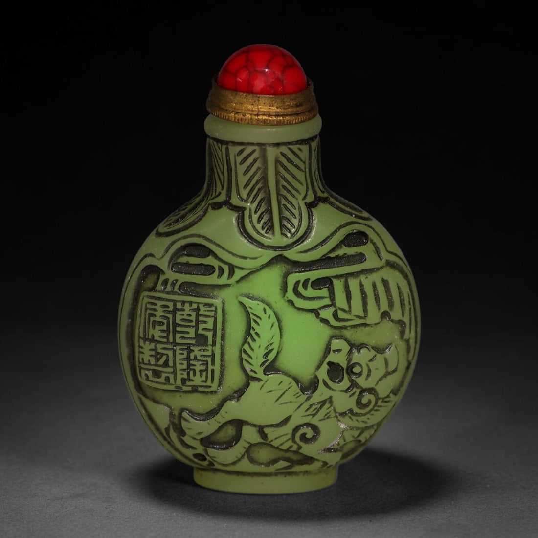 A Chinese Phosphorescent Green Relief Carved Fu Lion Snuff Bottle, 86AV: Globular phosphorescent green snuff bottle, the material glows neon in the dark when illuminated by torch light, deeply relief-carved with fu lion motif alongside an inscribed seal mark within a styli