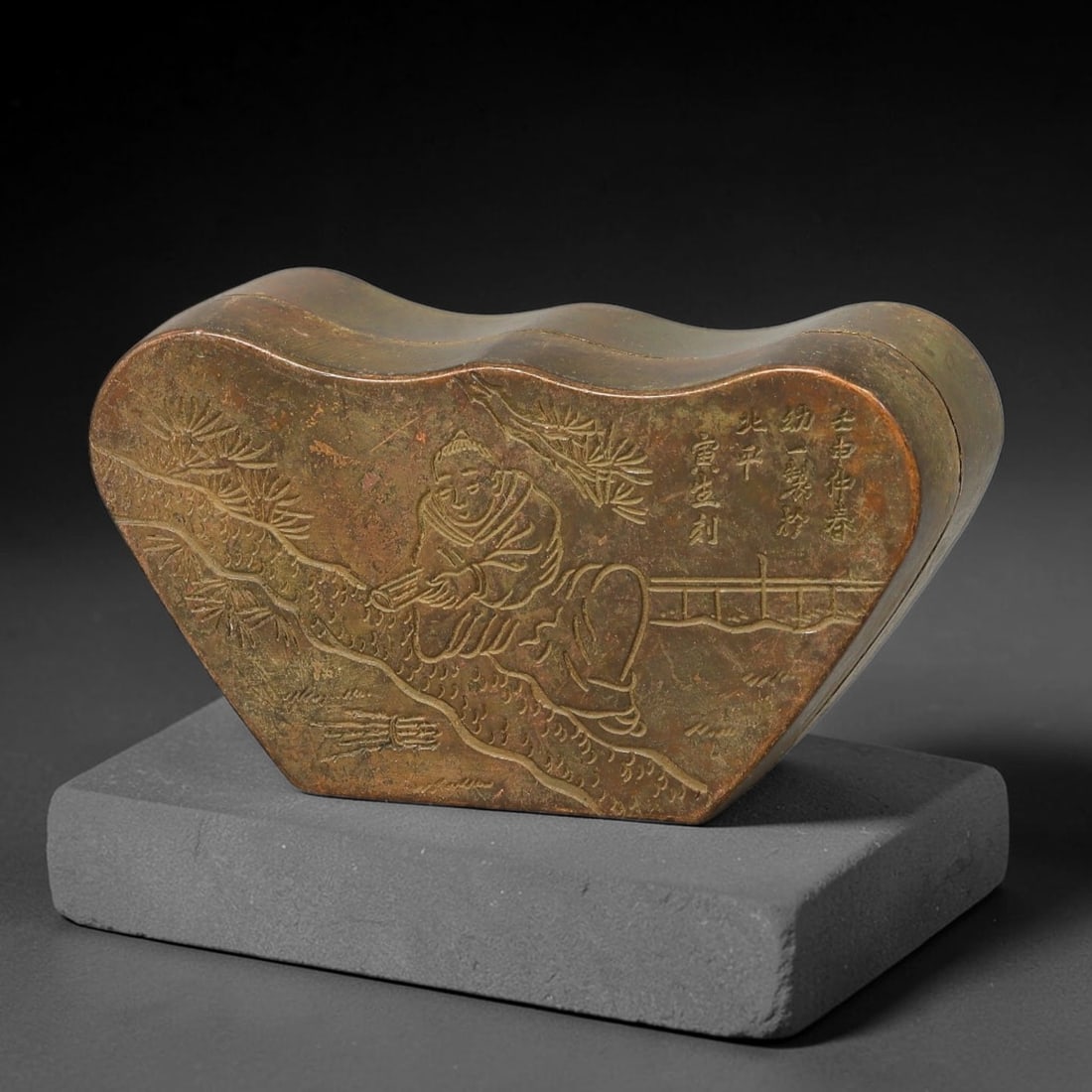 A Chinese Late Qing Dynasty Bronze Ingot-Form Snuff Box, 84AX: Cast bronze ingot-shaped container with a fitted lid. The lid surface carries incised decoration depicting a reclining figure beneath pine branches, paired with vertical columns of carved Chinese insc