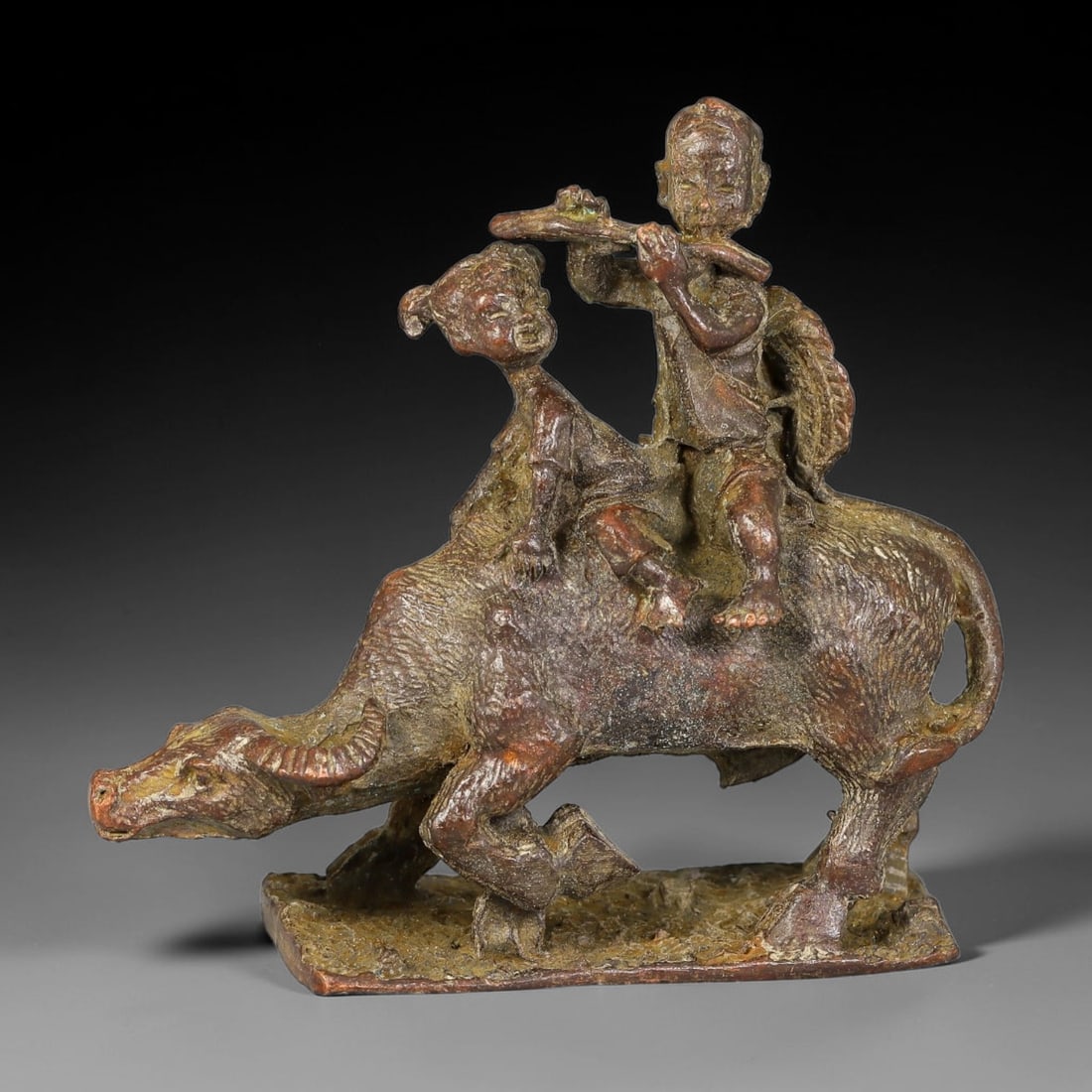 A Chinese Bronze Buffalo with Two Boys Figurine, 23AX: Cast bronze group depicting two boys riding atop a walking buffalo. One boy plays a flute while the other leans beside him; the buffalo is rendered with textured hide, curved horns and detailed hooves
