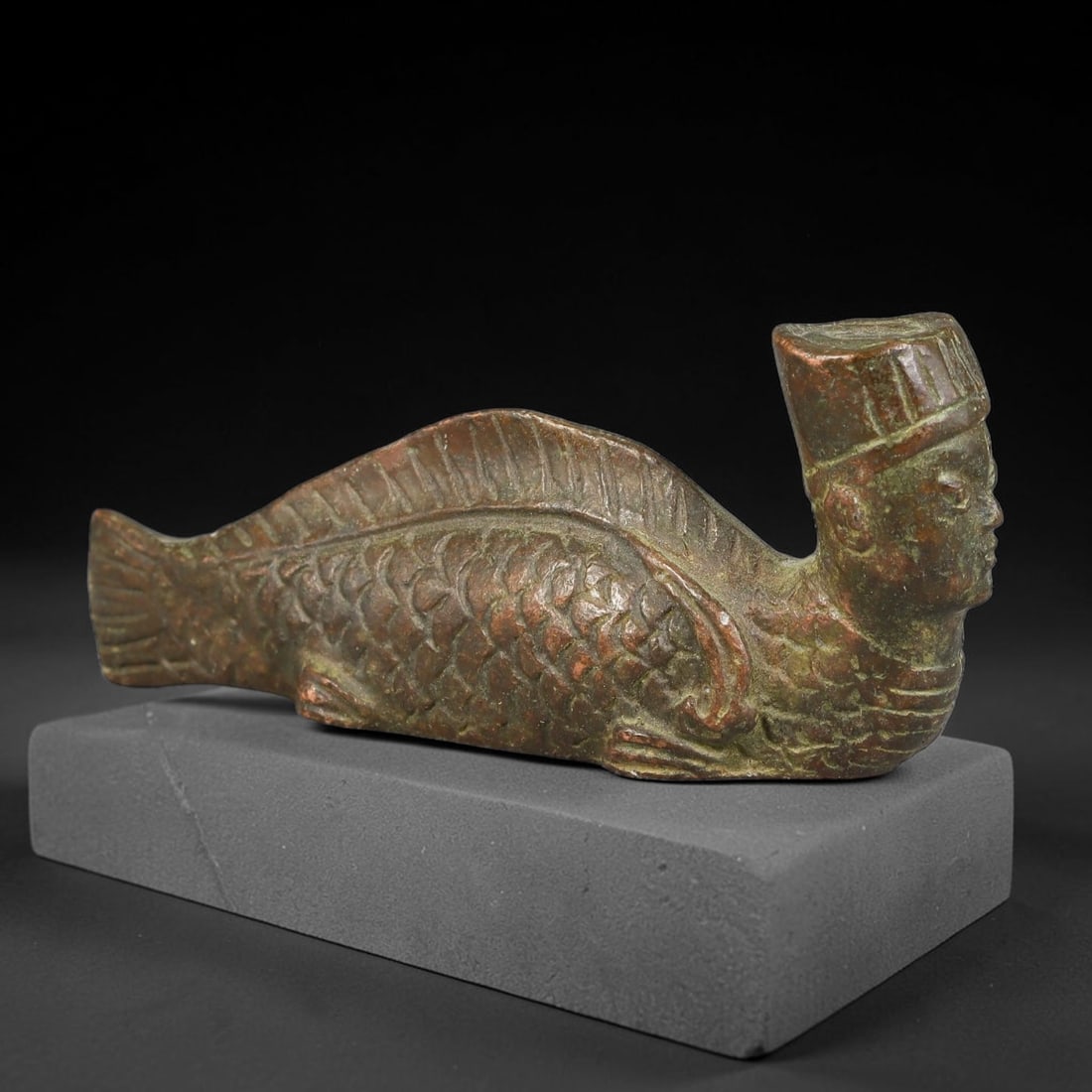A Chinese Bronze Archaic Style Human-Headed Mermaid Mythical Creature Figurine, 45AX: Cast bronze mythical mermaid creature featuring a human head wearing a stylized cap seamlessly joined to a fully scaled fish body with defined dorsal, pectoral and tail fins. Fine incised detailing re