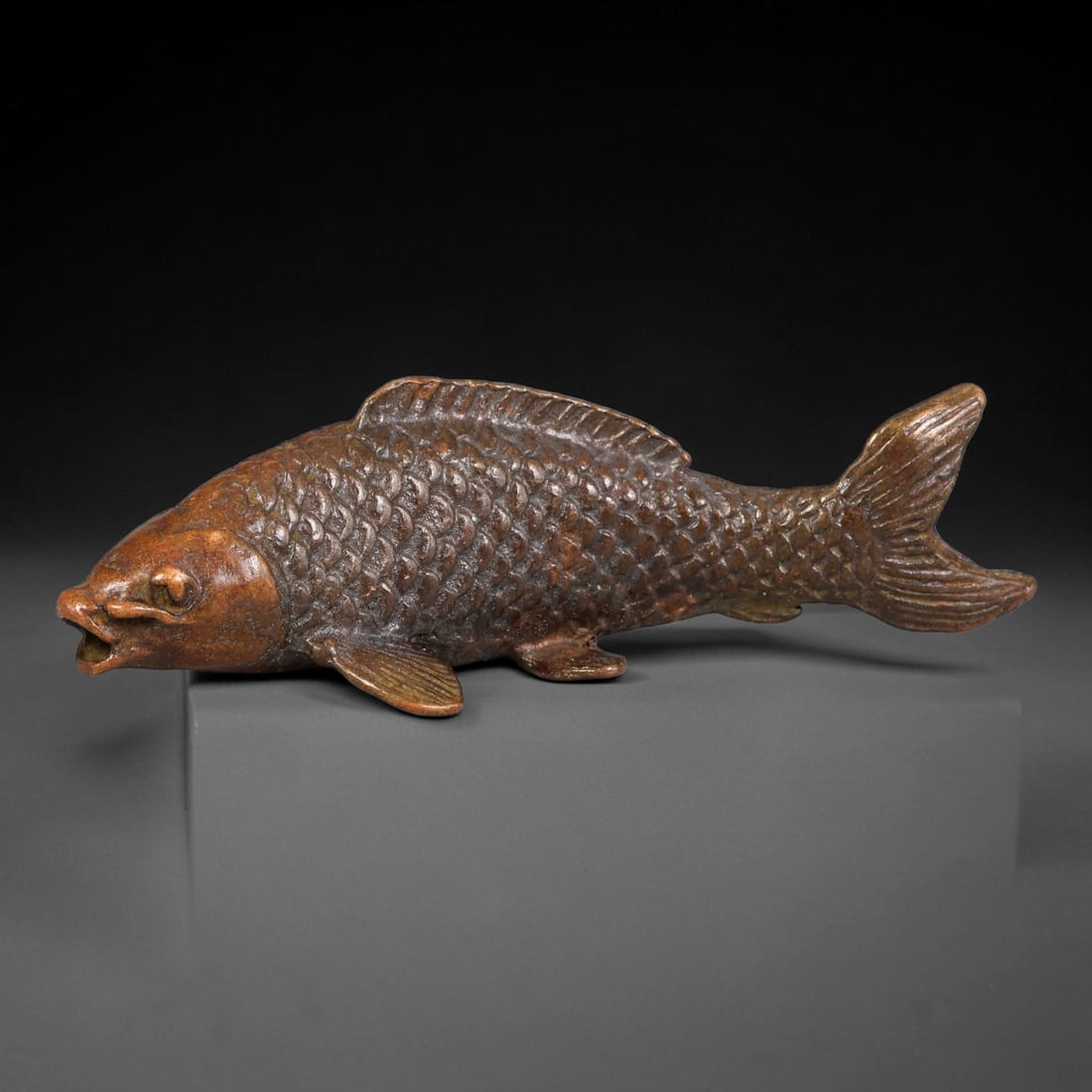 A Chinese Bronze Naturalistic Carp Ornament, 42AX: Cast bronze carp finely modelled with individually defined scales, detailed pectoral, dorsal and tail fins, and a gently open mouth, capturing the fluid form of the fish. The bronze has a rich deep ag