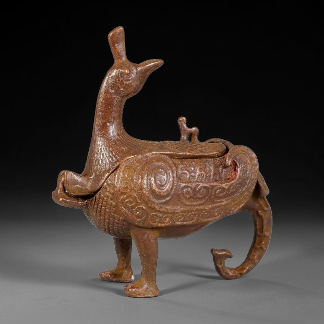 A Chinese Bronze Archaic Style Phoenix Censer, 46AX: Cast bronze censer modelled as a standing phoenix bird, with hinged lid integrated into its back, raised crest and elegantly curved tail. The body is decorated with fine raised scale and spiral relief