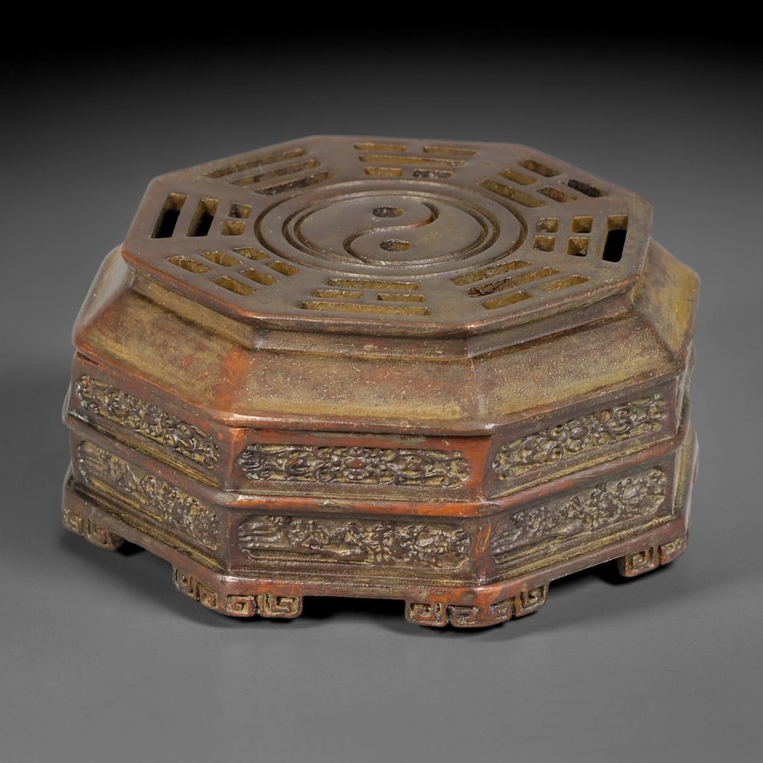 A Chinese Bronze Octagonal Bagua Censer, 80AX: Cast bronze octagonal lidded censer. The pierced lid features a central yin-yang symbol surrounded by trigrams of the bagua. The body is decorated with continuous carved floral and scroll relief bands