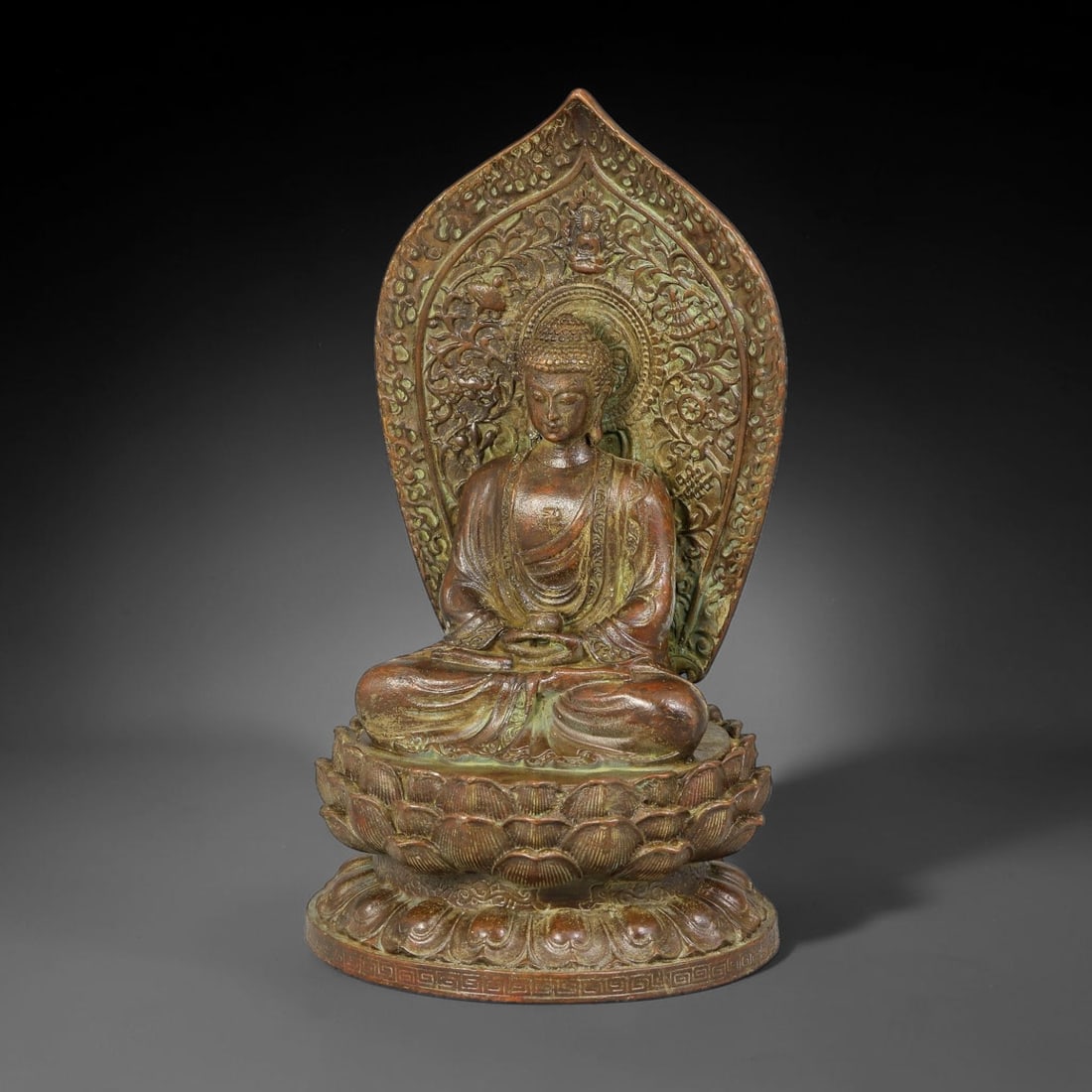 A Chinese Bronze Seated Buddha Statue, 77AX: Cast bronze figure of Buddha seated in meditation pose upon a double lotus pedestal, holding an alms bowl. The large mandorla behind the figure is richly decorated with relief floral scrollwork and sm