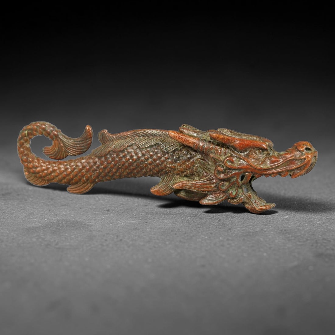 A Chinese Bronze Dragon Fish Effigy, 47AX: Cast bronze effigy modelled as a dragon fish, with detailed scaled body, fin detailing and fully modelled dragon head. The bronze surface bears rich aged patina and subtle surface abrasion. Height 2 c
